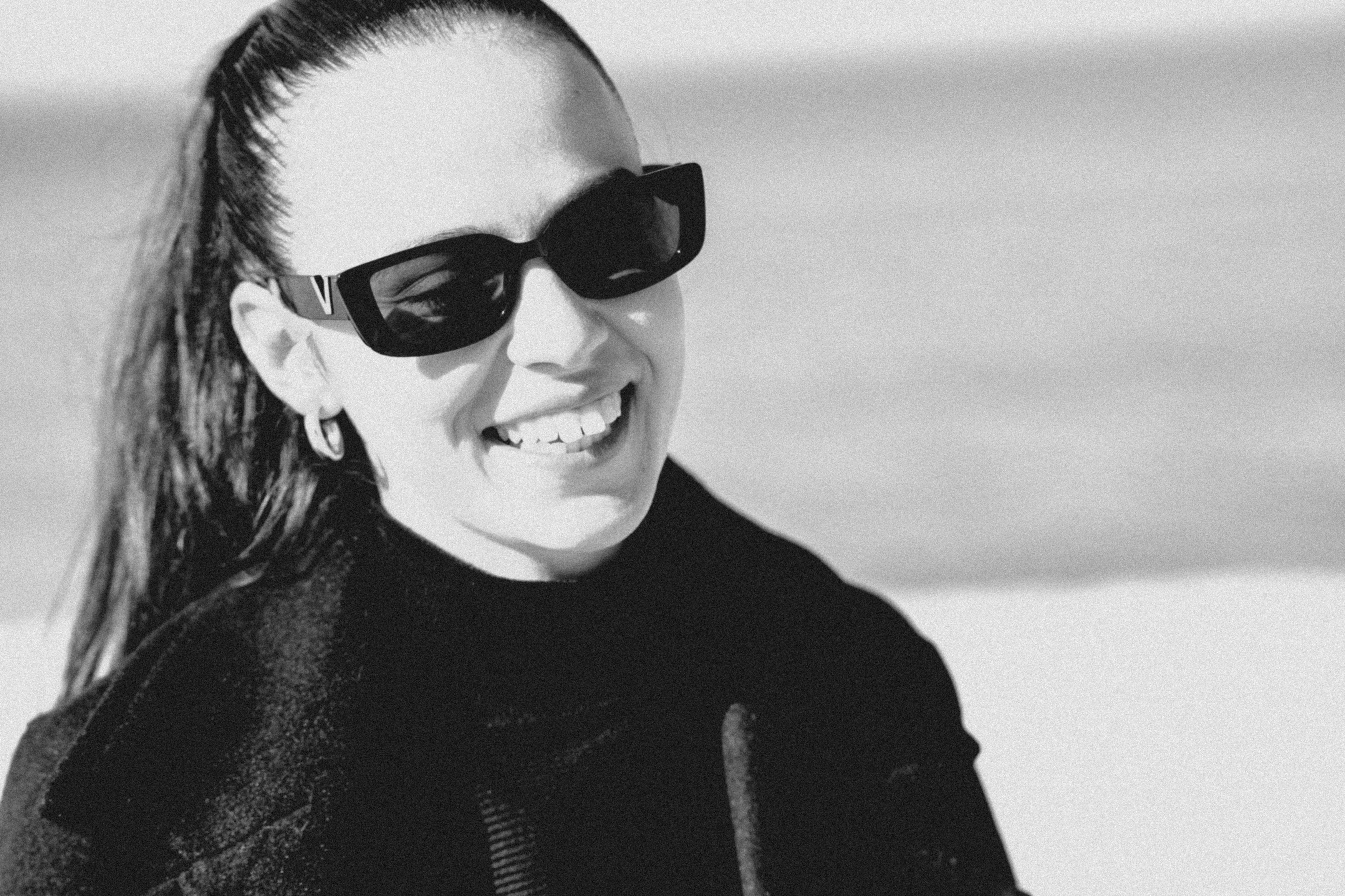 Wanita mengenakan kacamata hitam dan tersenyum di luar ruangan