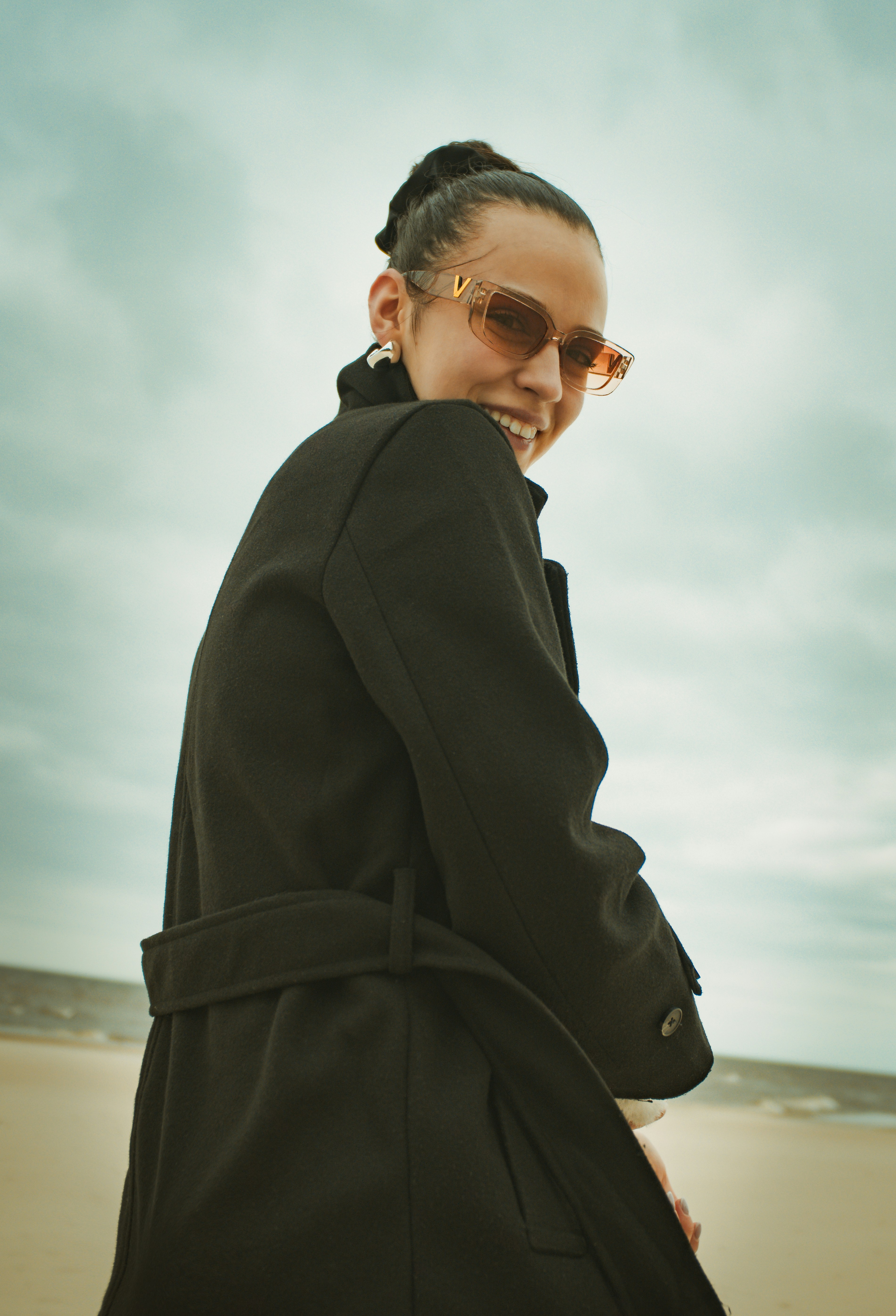 Frau im schwarzen Mantel lächelt am Strand
