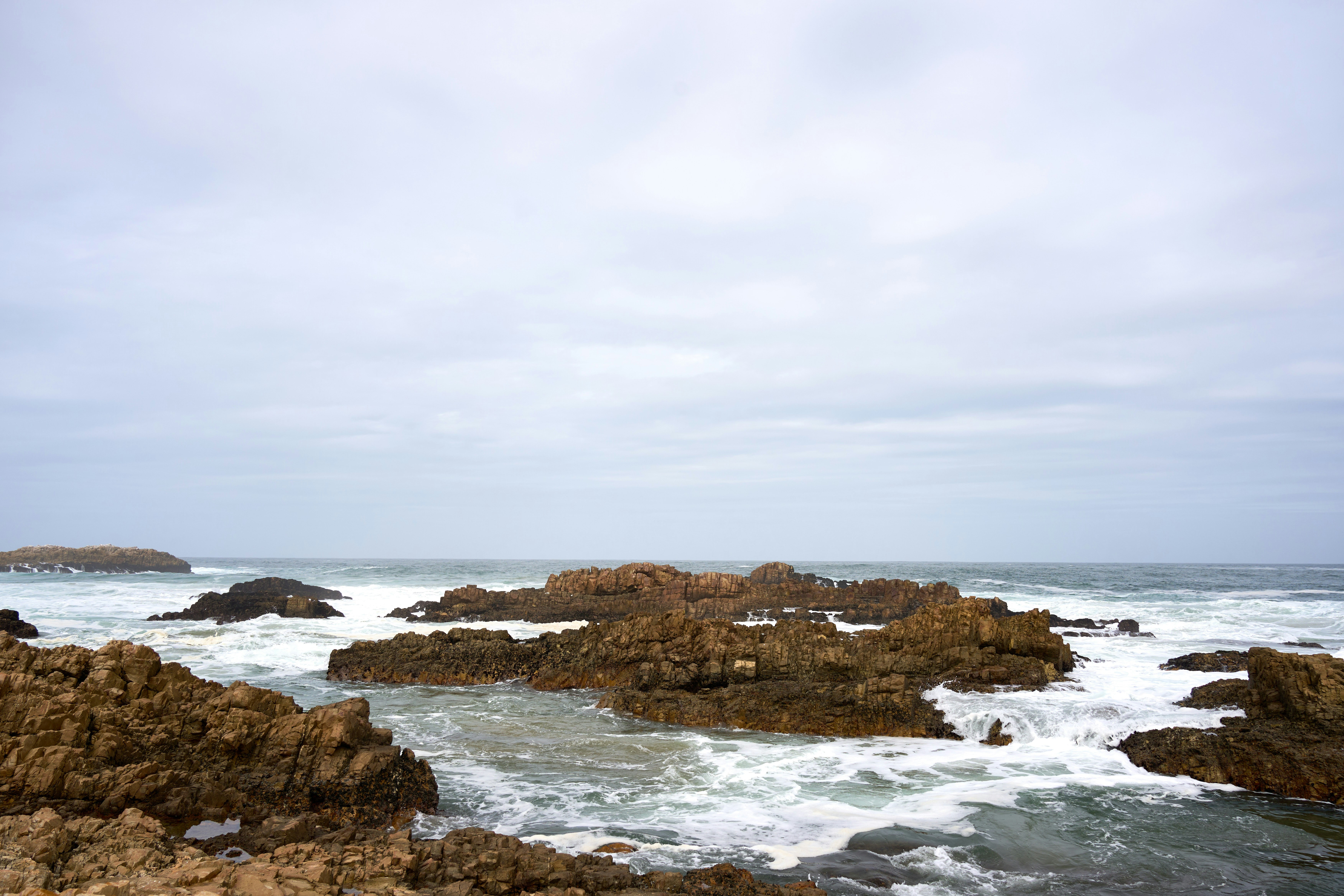 흐린 하늘 아래 바위 해안에 파도가 부딪힌다