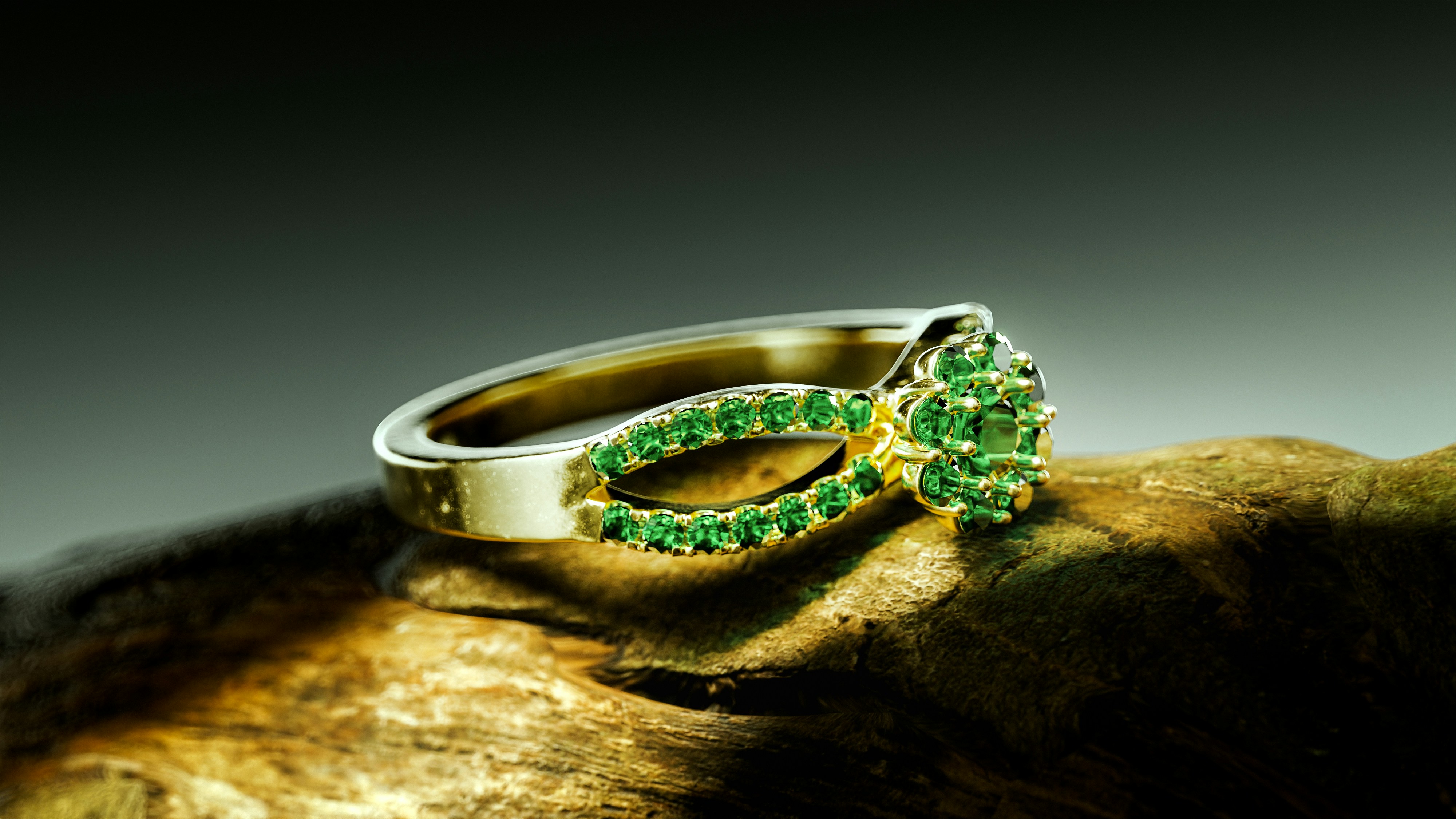 A gold ring with green gemstones on wood