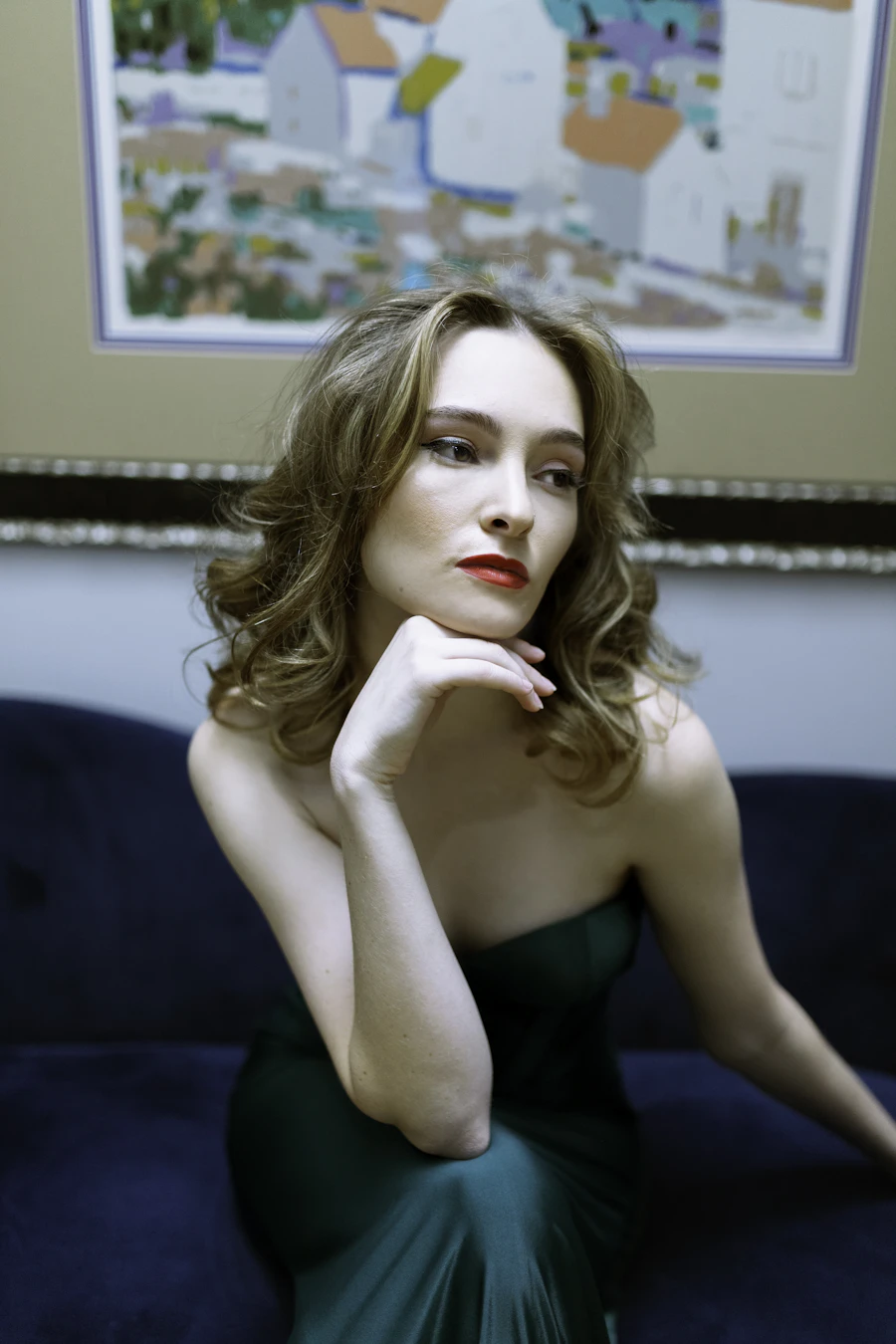 Model in an emerald gown seated beneath framed art