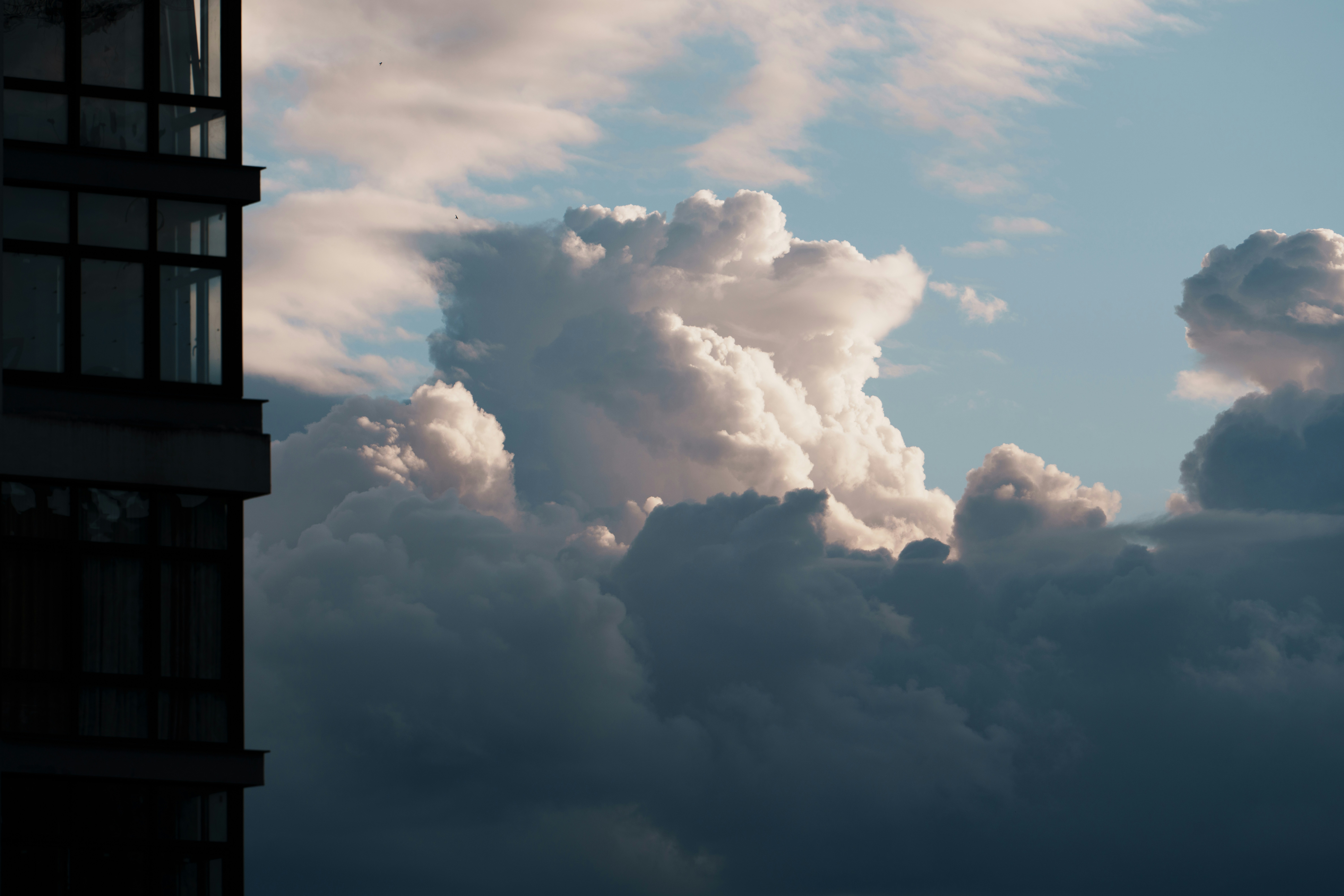 Dramatic clouds illuminated by sunlight next to building.