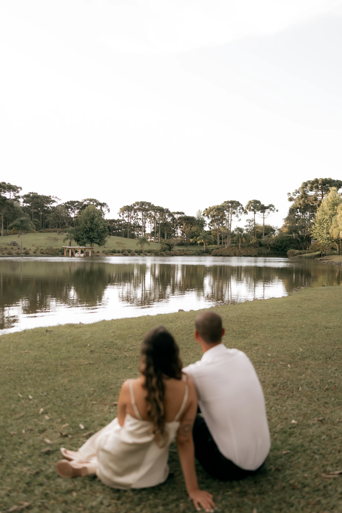 Couple relaxing together on green grass overlooking a calm reflective lake in an urban park setting