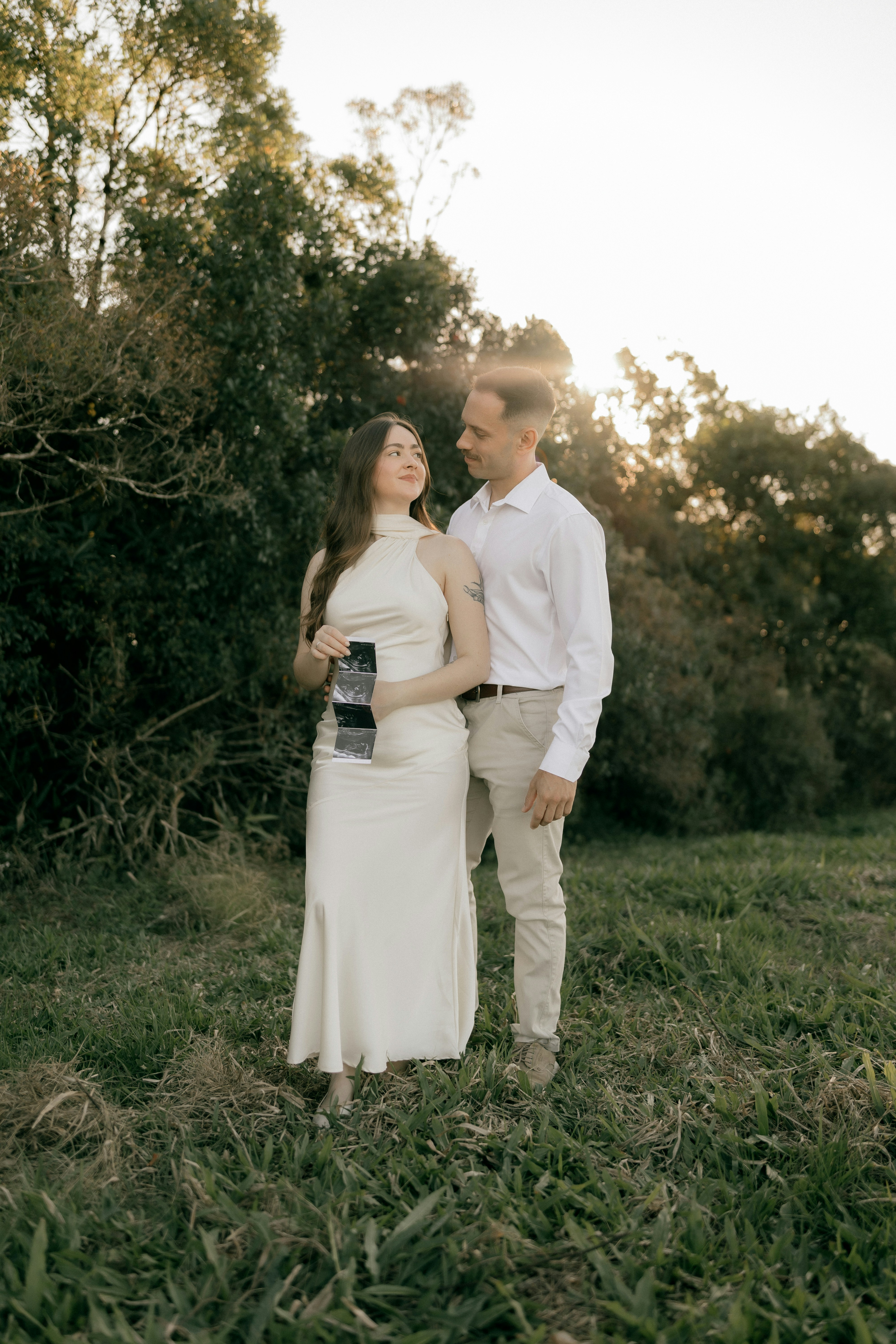 Couple holding ultrasound picture in a grassy field.
