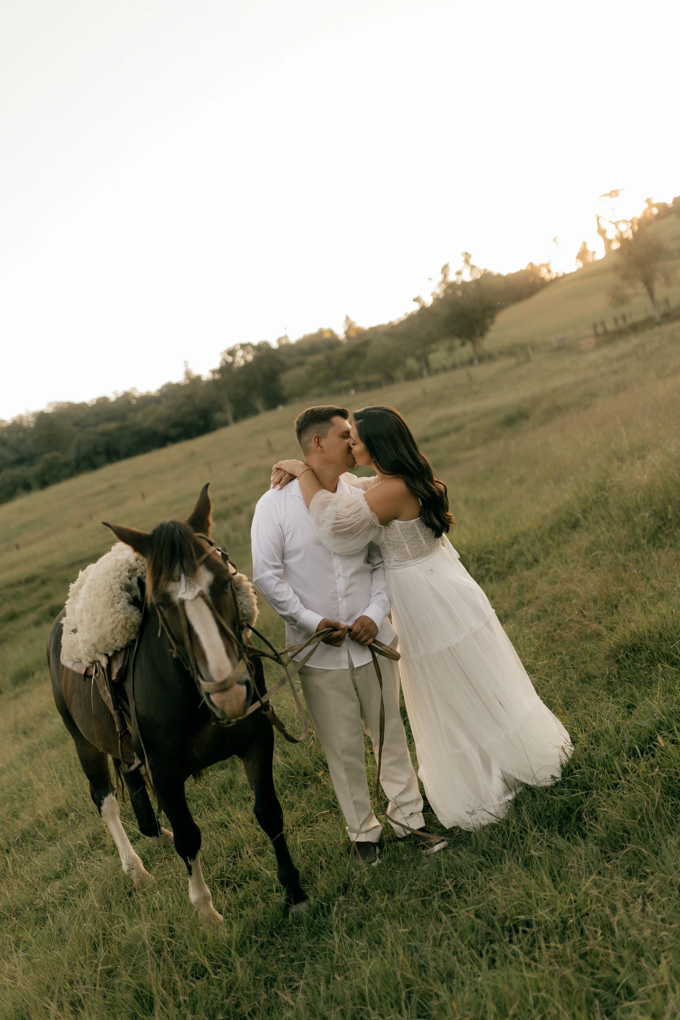 Couple in elopement attire under the apple blossom canopy of a Prince Edward County orchard in late April with the white blossoms covering the branches above them