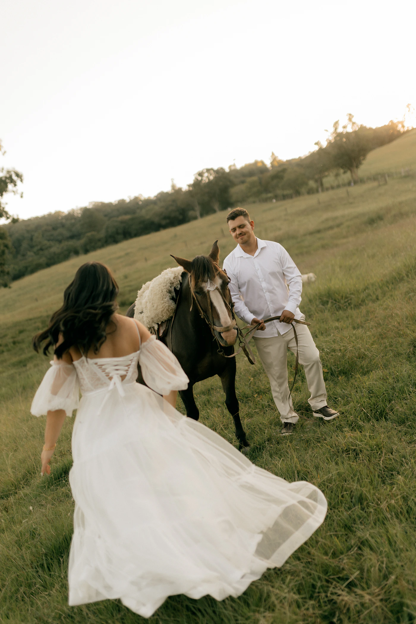 Couple in elopement attire at a Prince Edward County winery with the vineyard rows and the pastoral farmland behind them during the harvest season