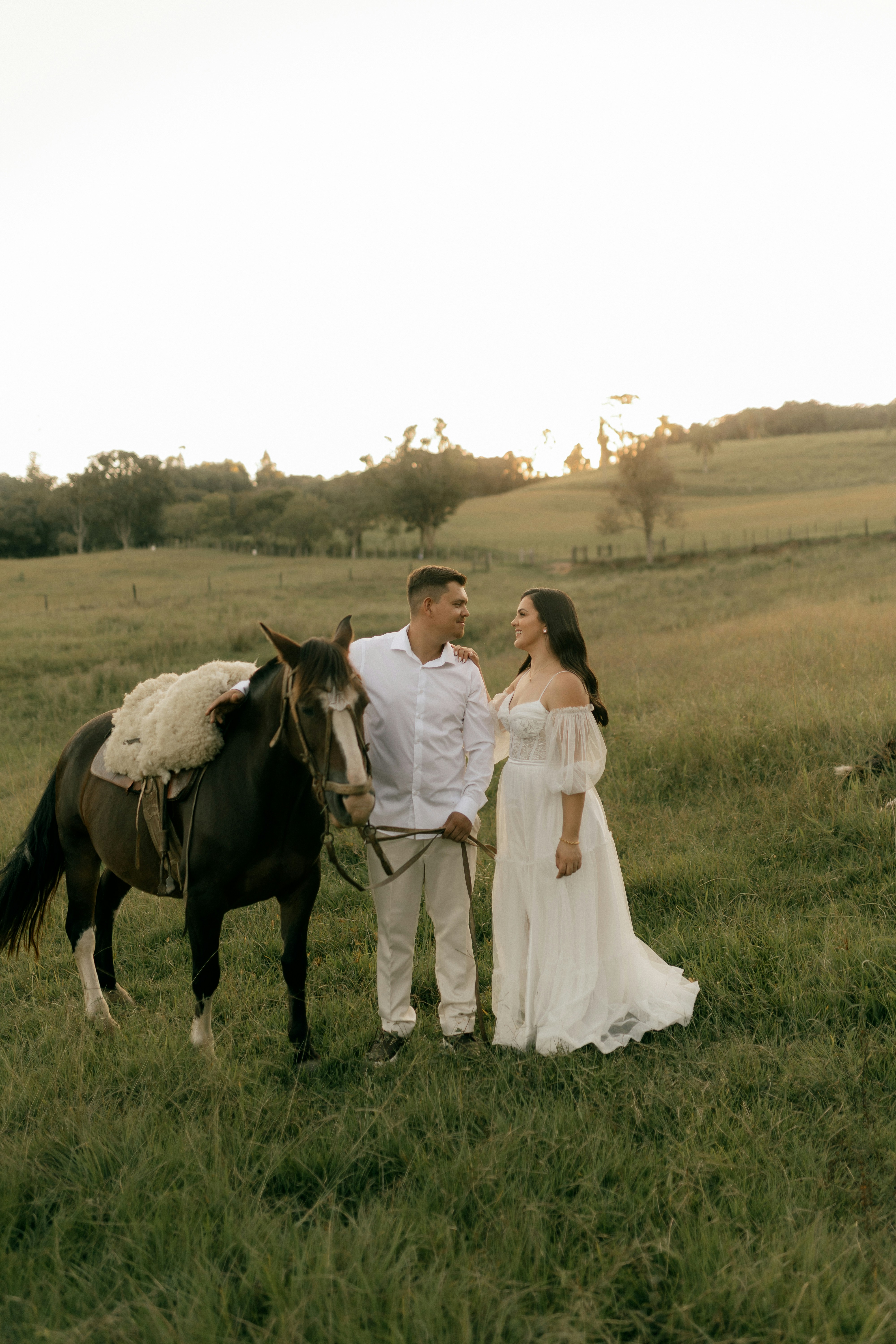 Couple with horse in a grassy field at sunset