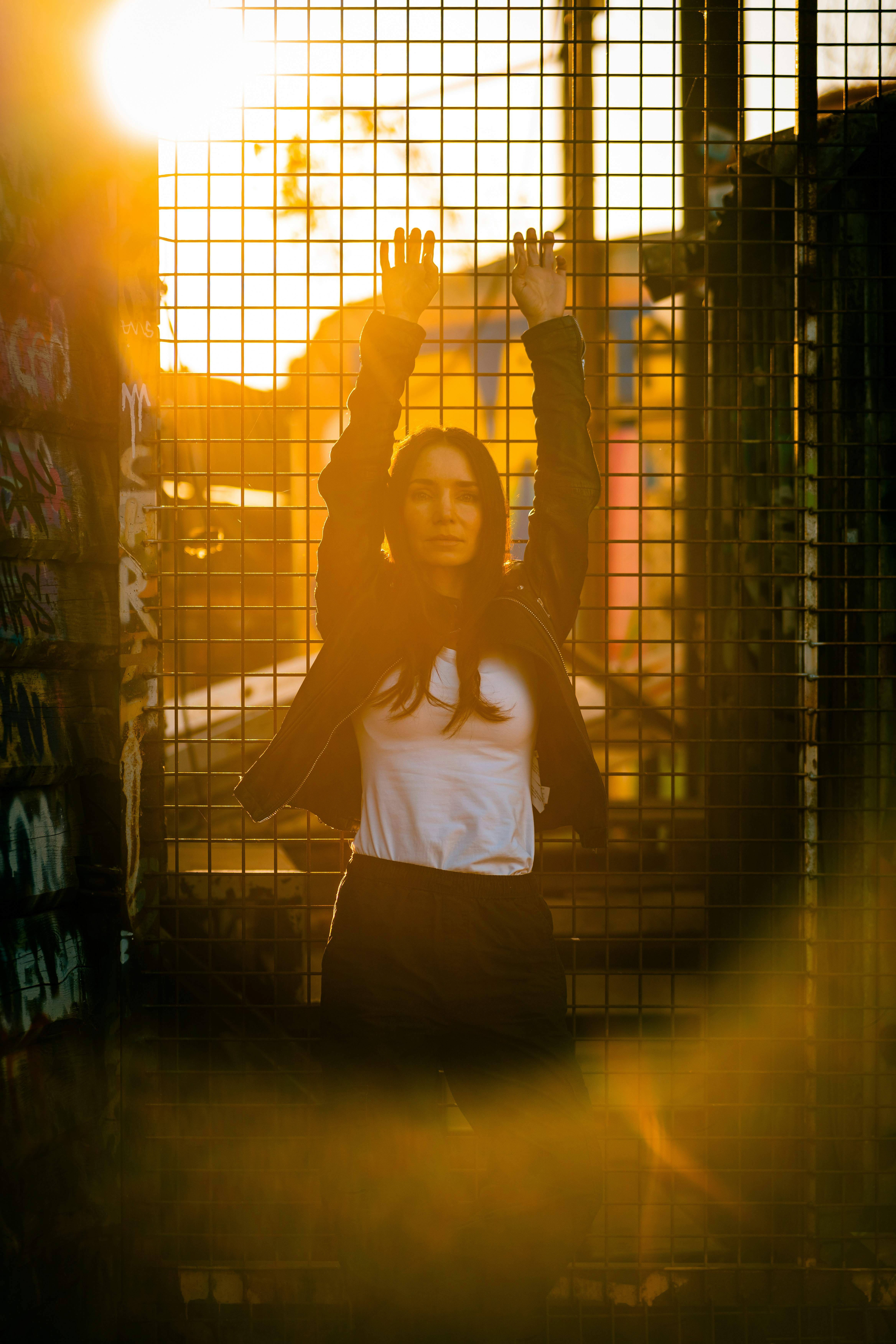 Woman with arms raised against a metal fence at sunset
