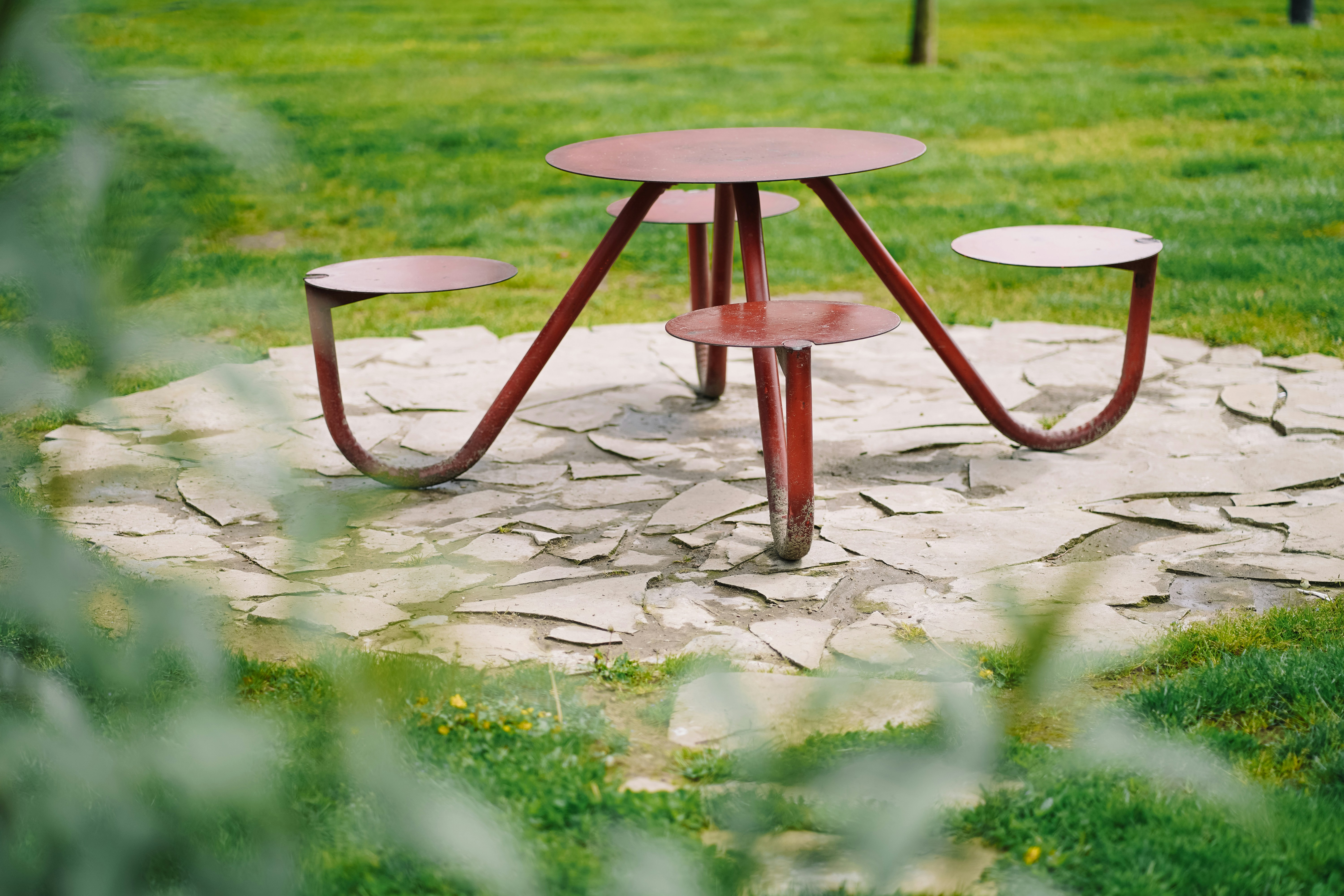 Mesa de piquenique vermelha em um pátio de pedra na grama.