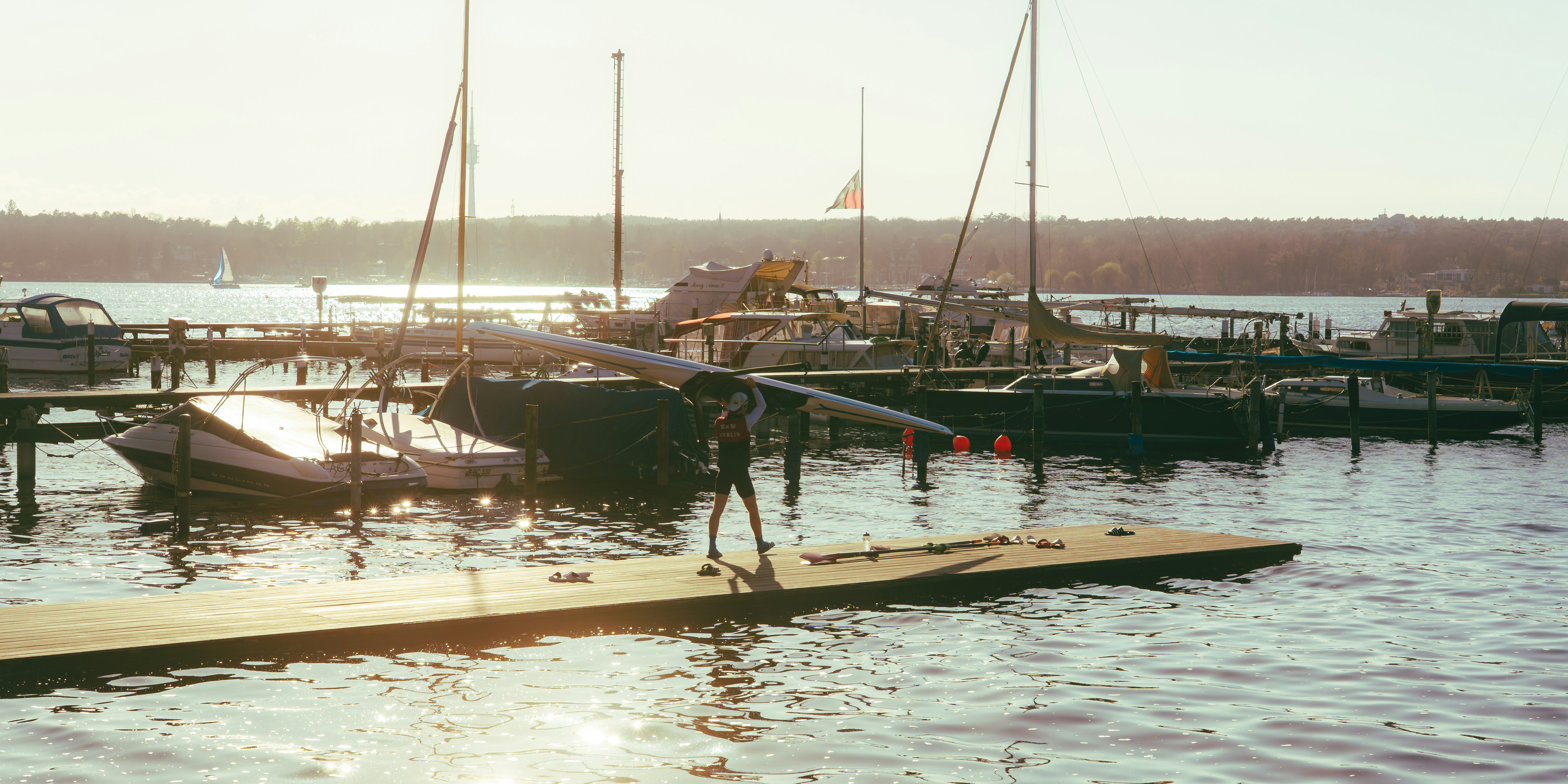 Man carries rowing shell on a dock at marina.