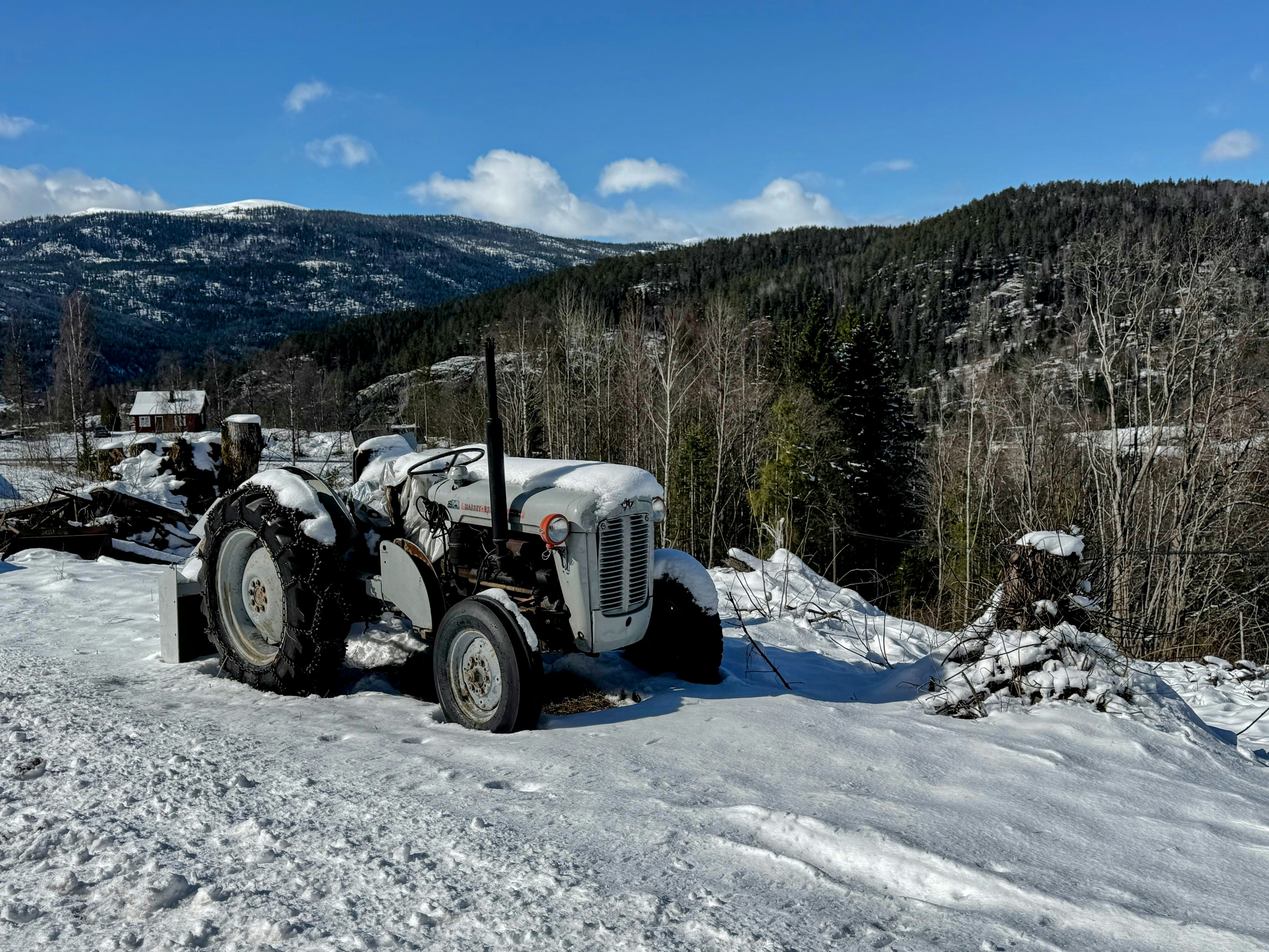 A white tractor sits in the snow with mountains behind