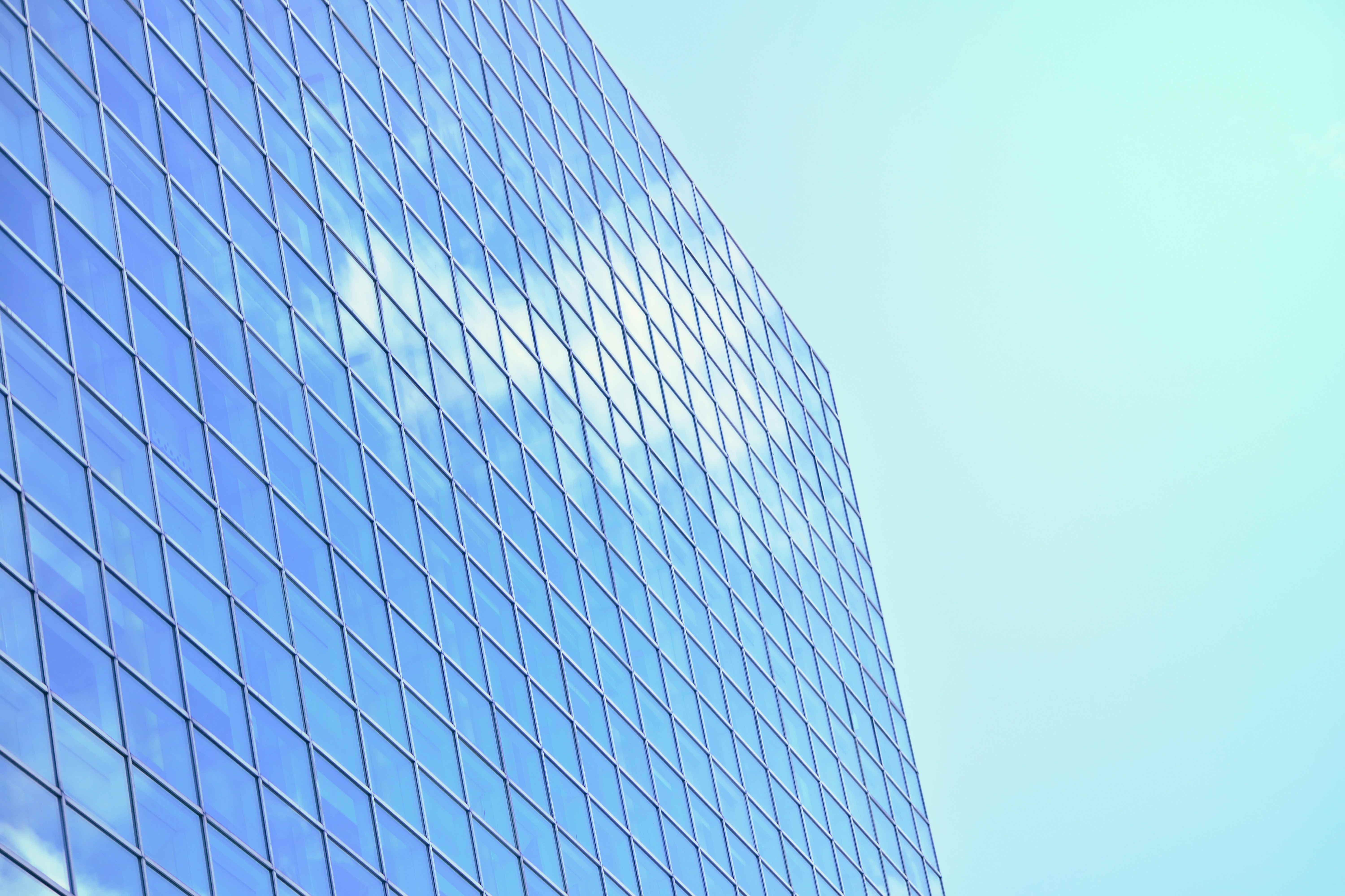 Modern glass building reflecting blue sky and clouds.