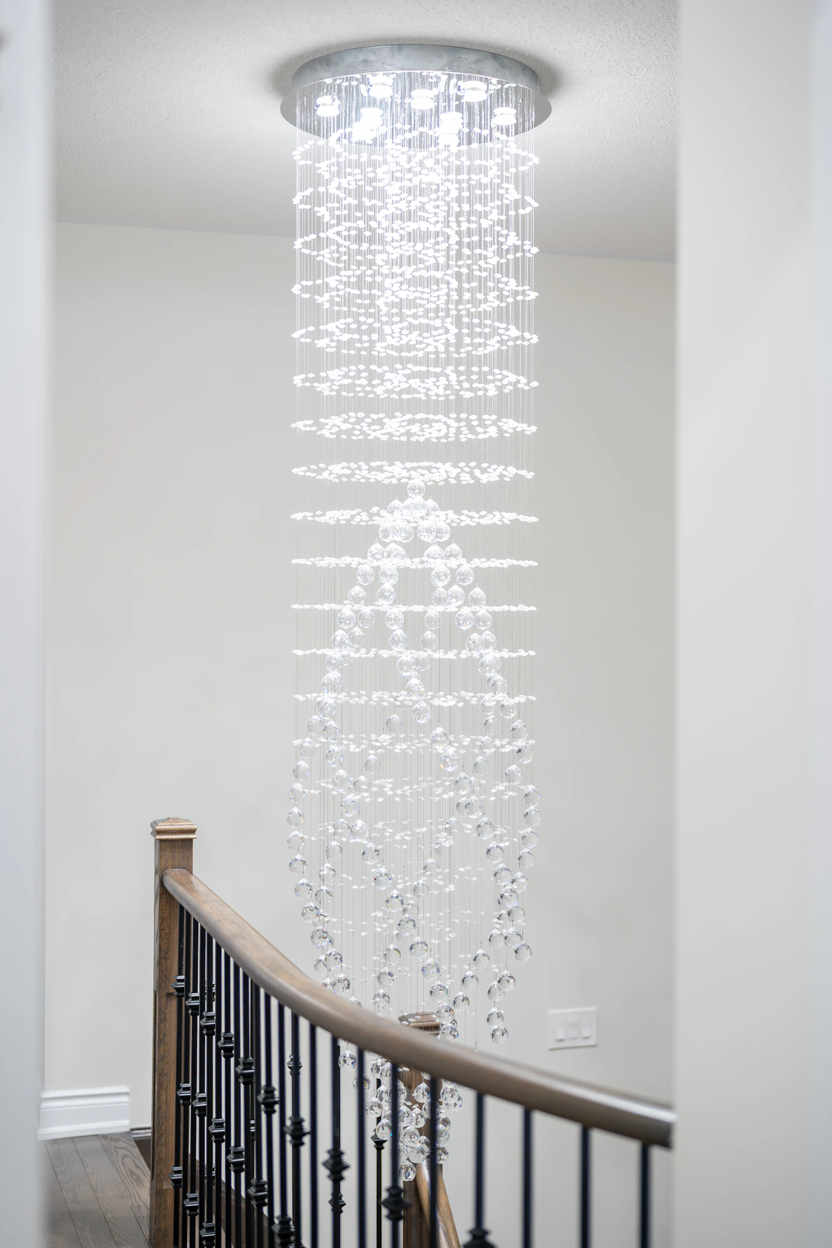 Long crystal chandelier over a staircase for comparing the fixture with the upper landing, railing, and tall window sightlines