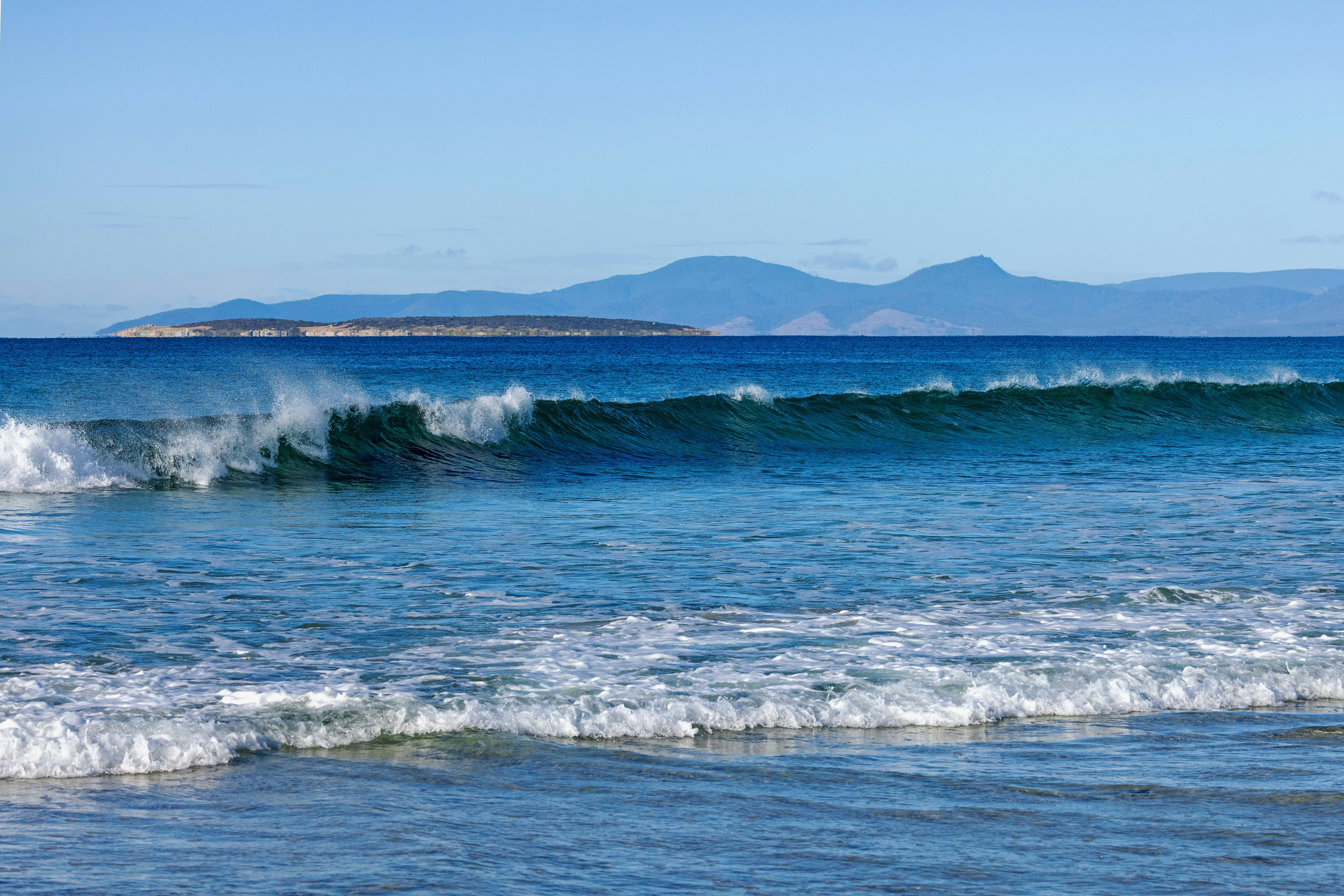 Waves crash on a beach with distant mountains.