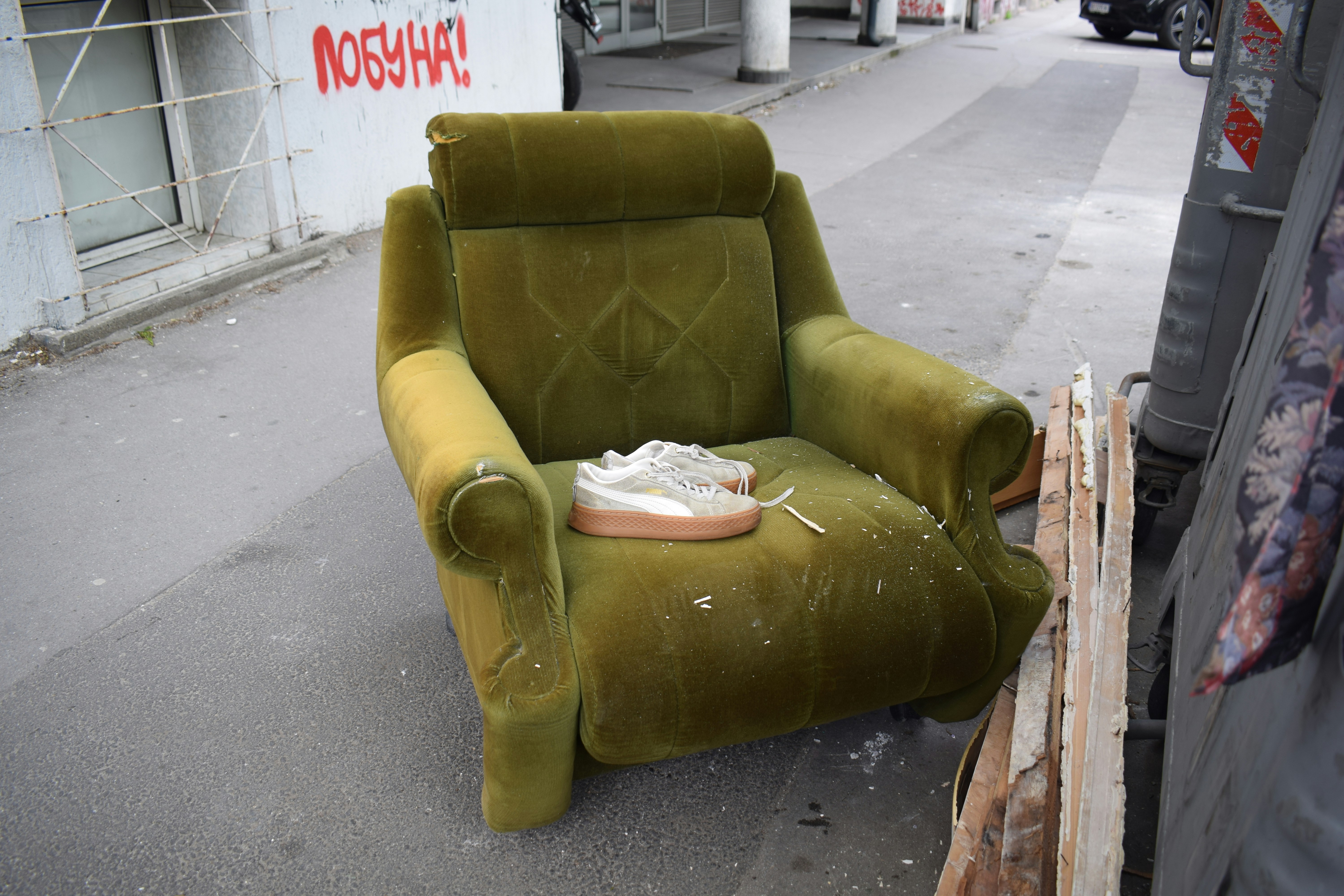An old green armchair sits on a sidewalk.