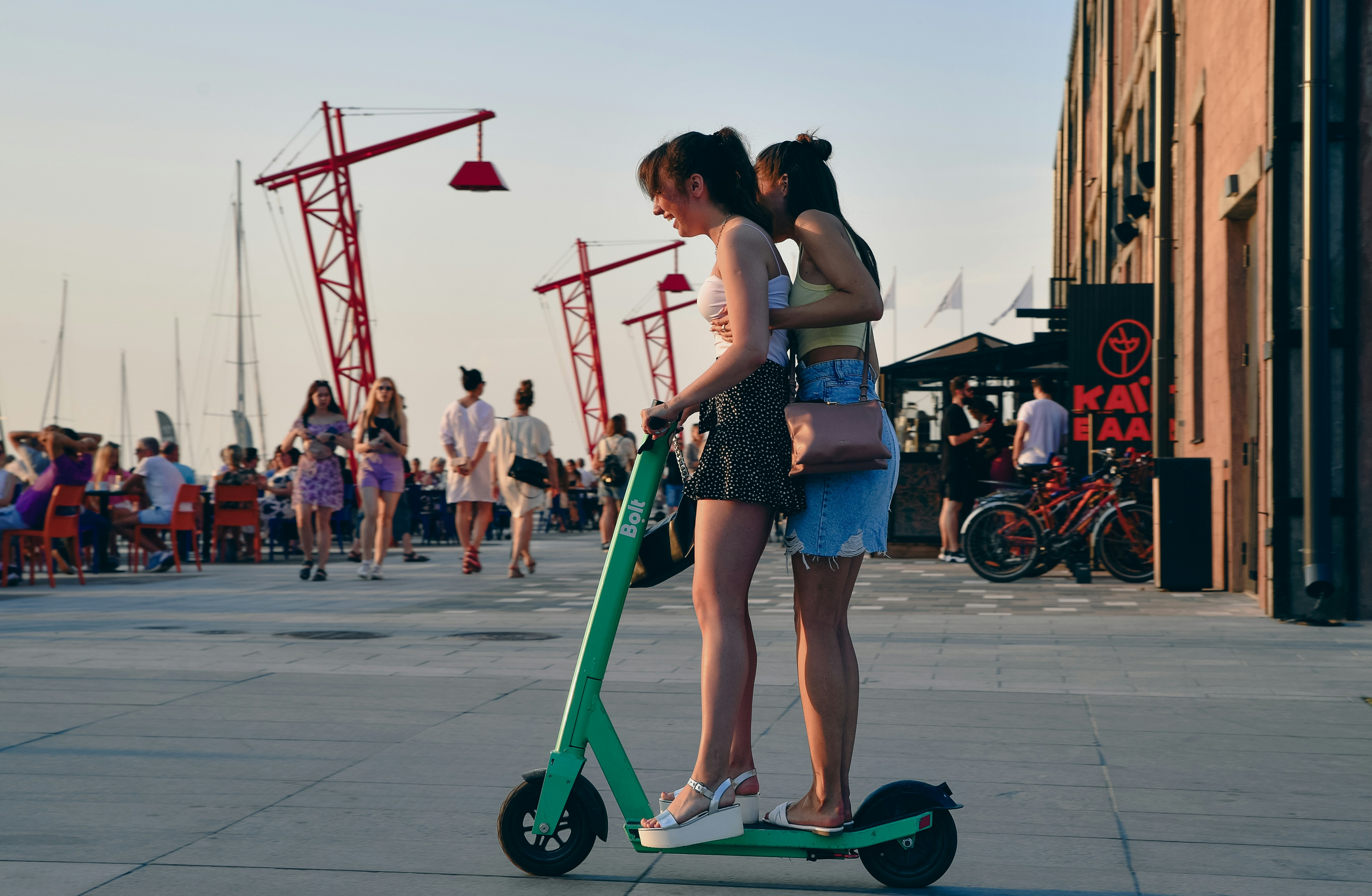 Two women share an electric scooter outdoors.