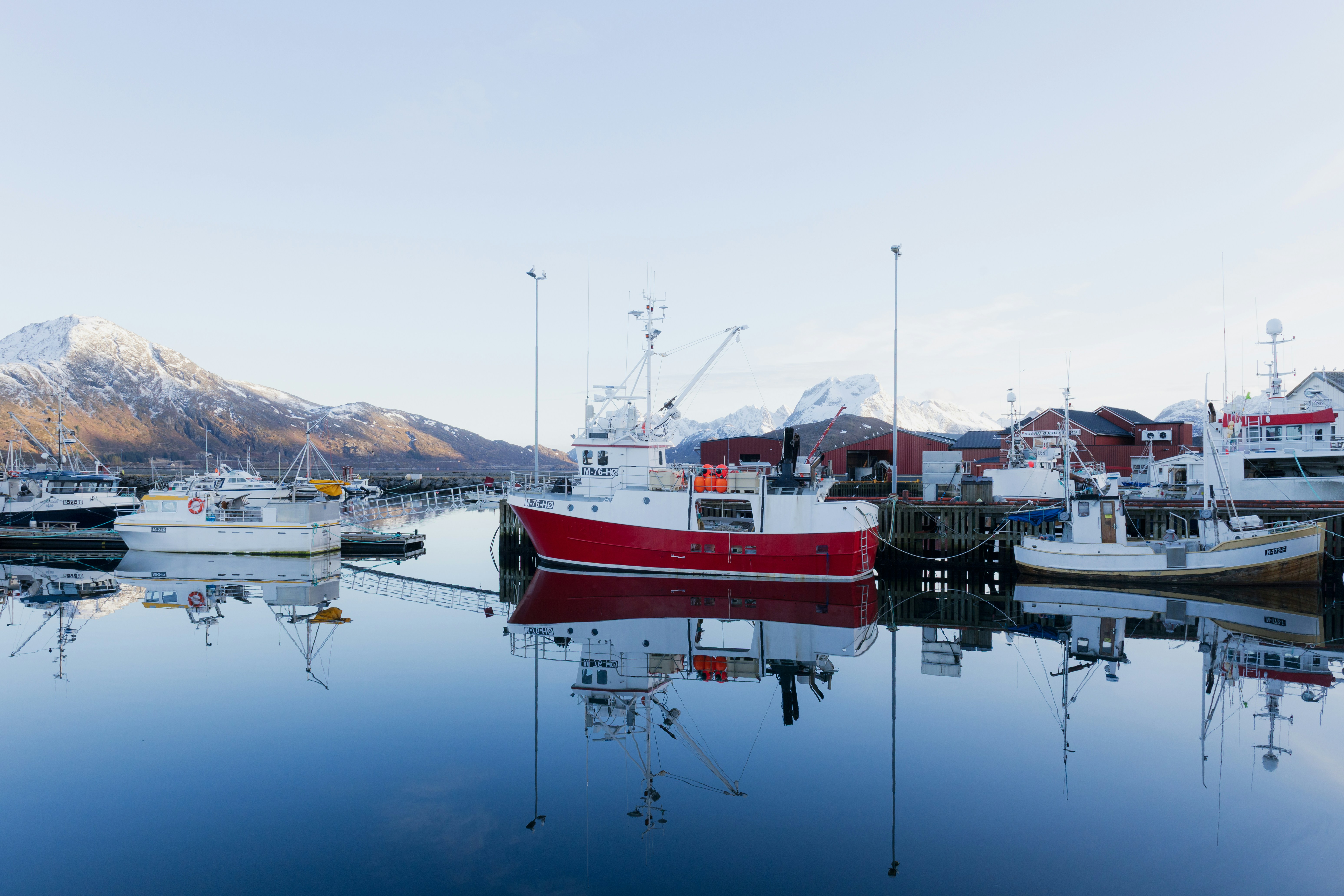 Fishing boats docked in a calm harbor with snowy mountains.