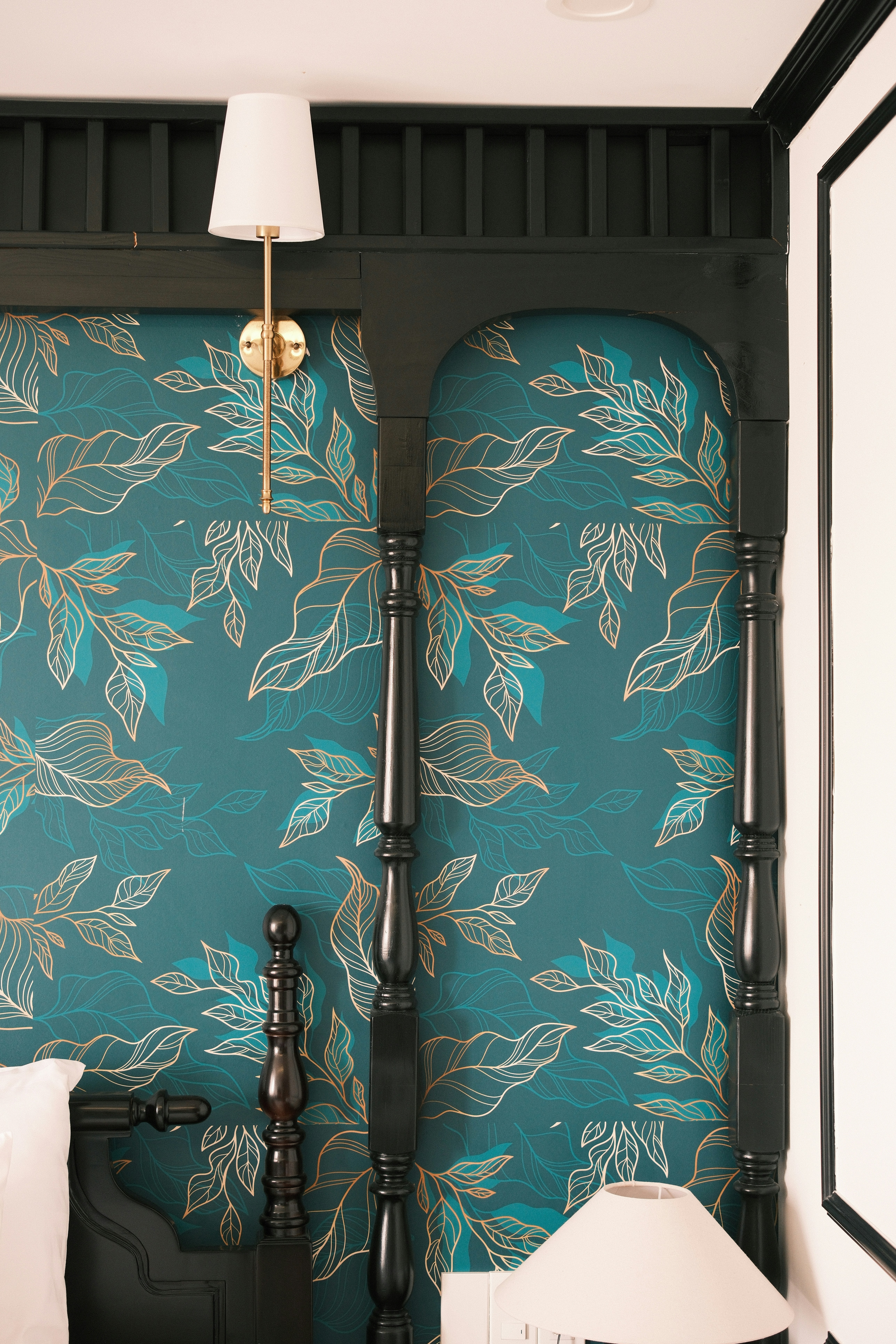 Dark wood bed frame against teal leaf patterned wallpaper.