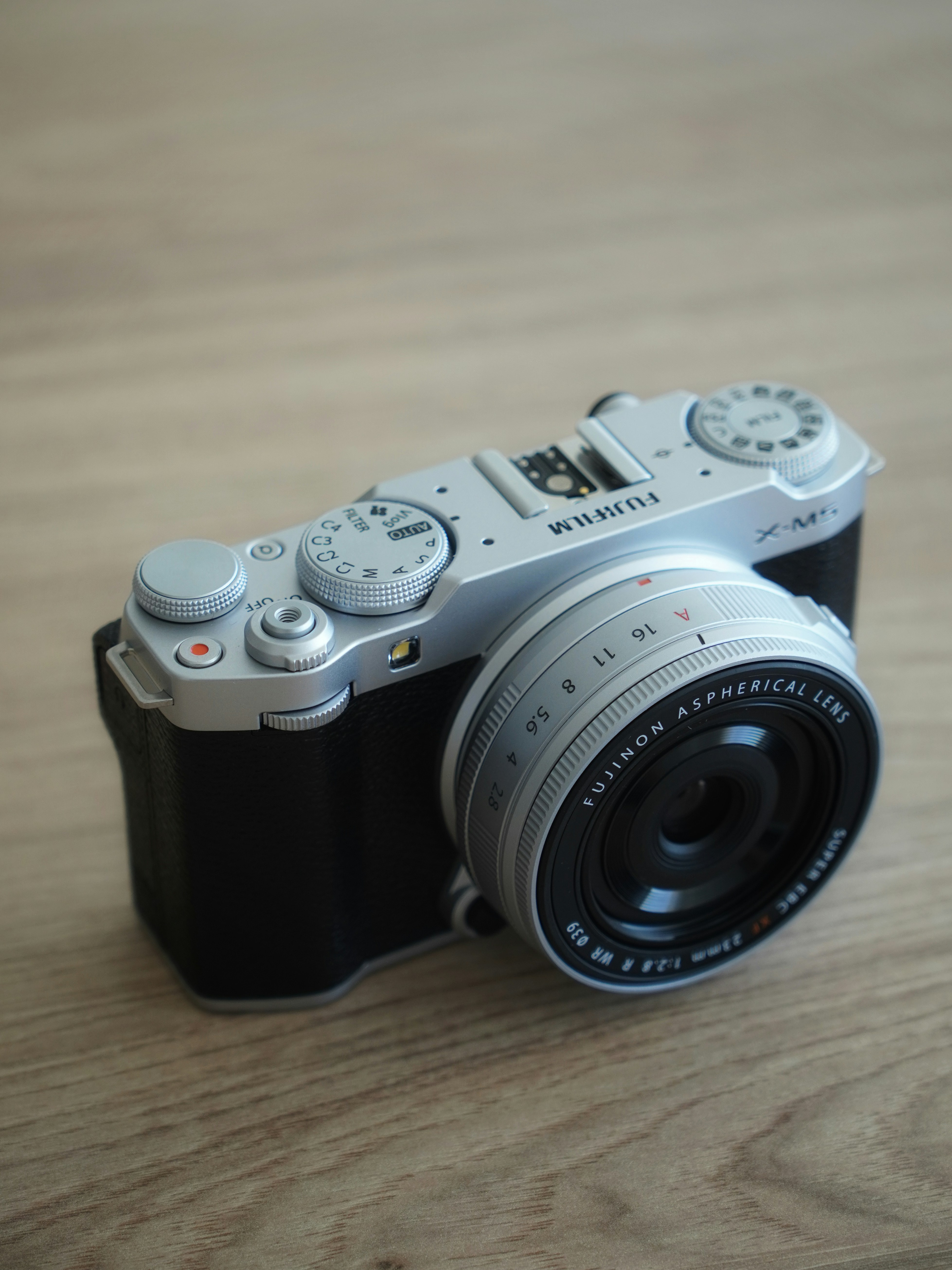 Silver fujifilm camera with black grip on wooden surface