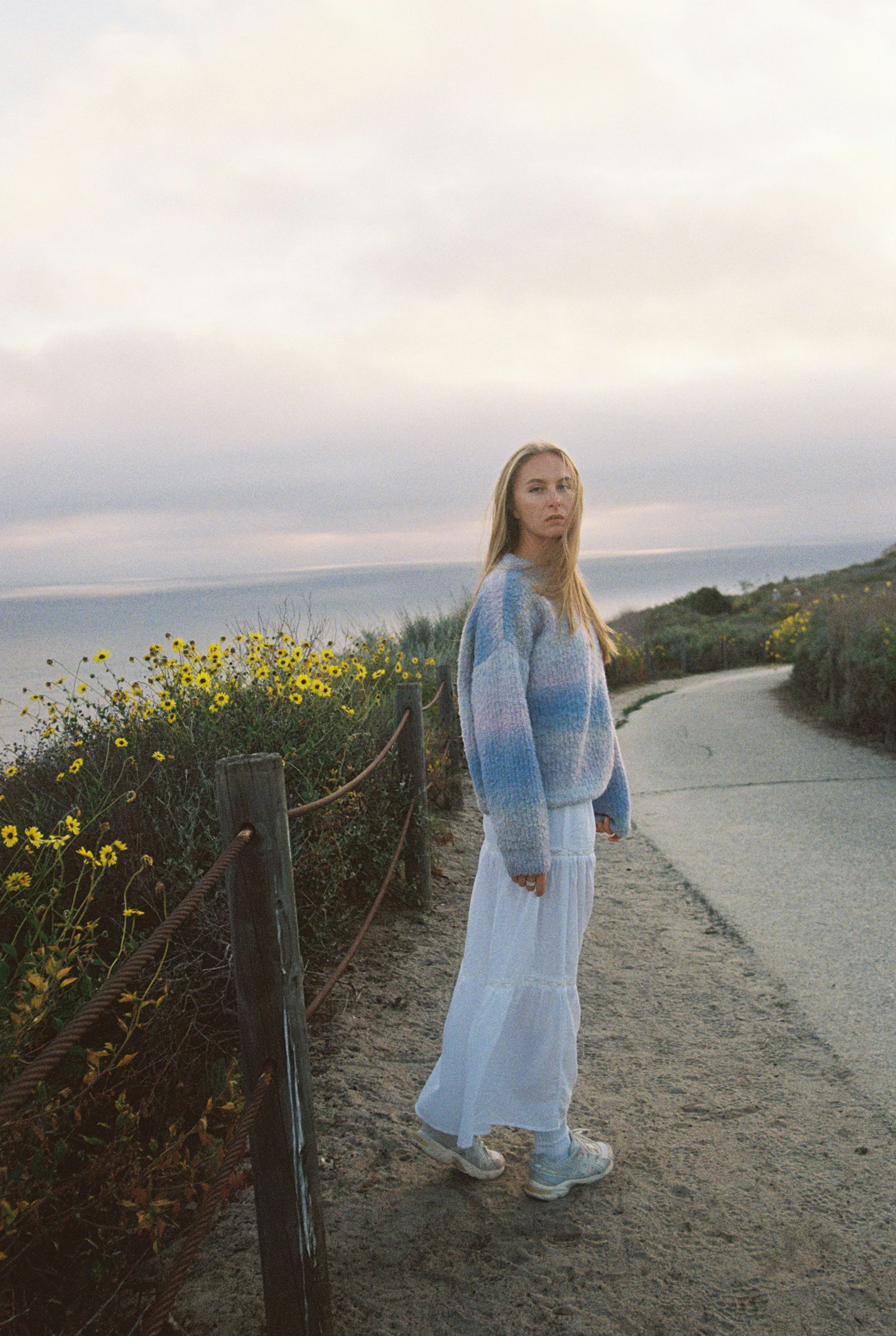 A young woman stands on a path by the ocean