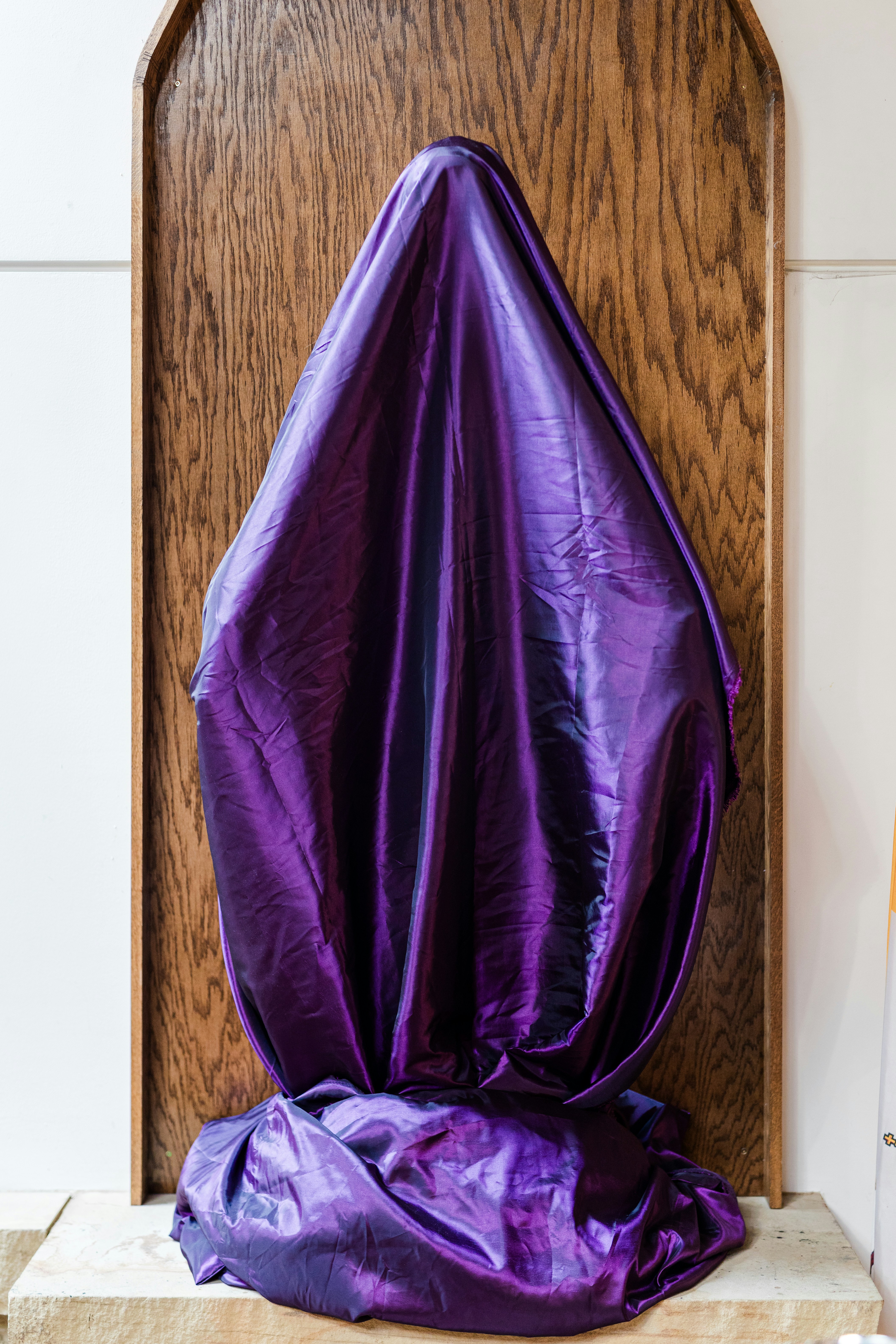 Una figura velada envuelta en tela morada se mantiene de pie.