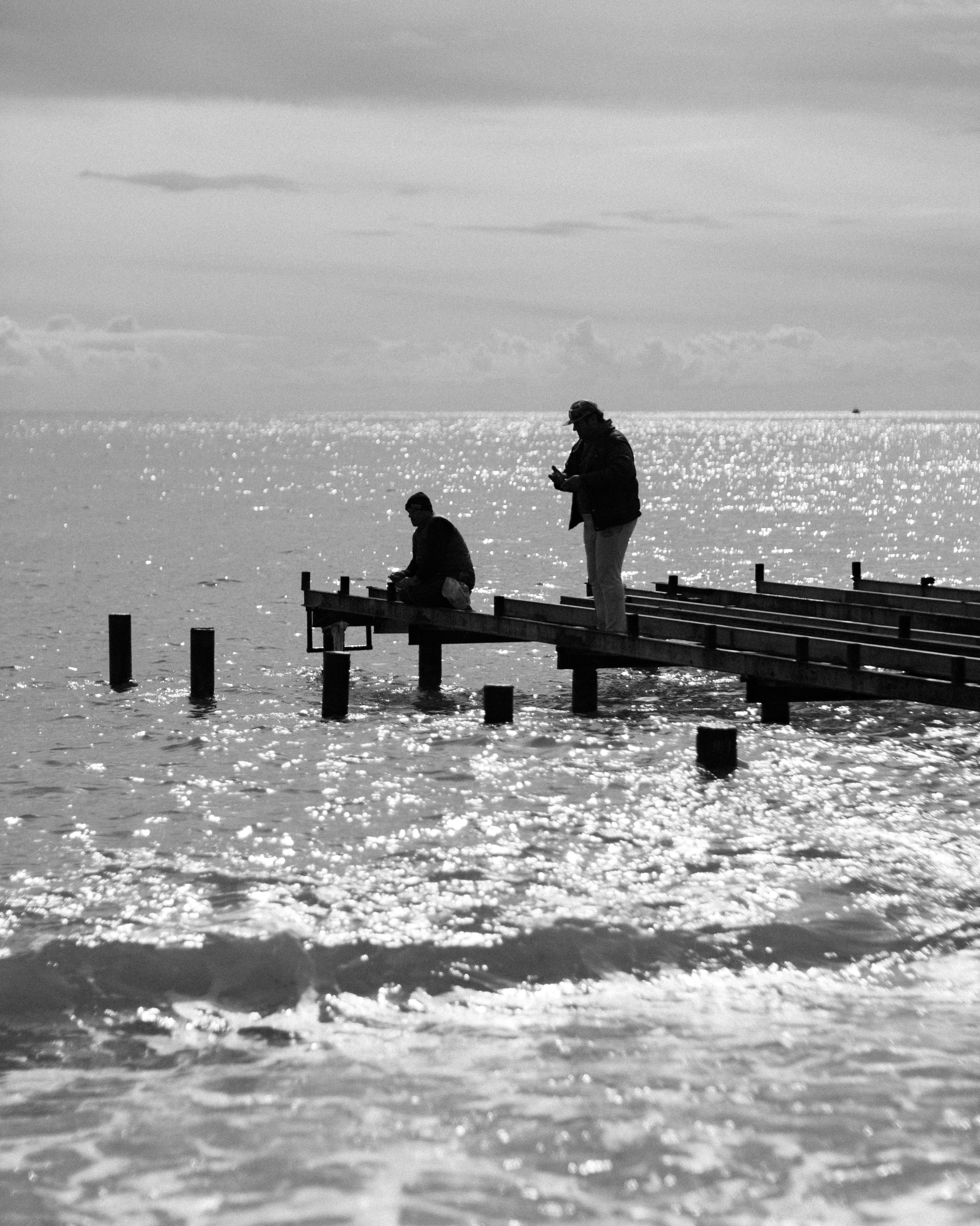 Two people on a pier by the sparkling ocean