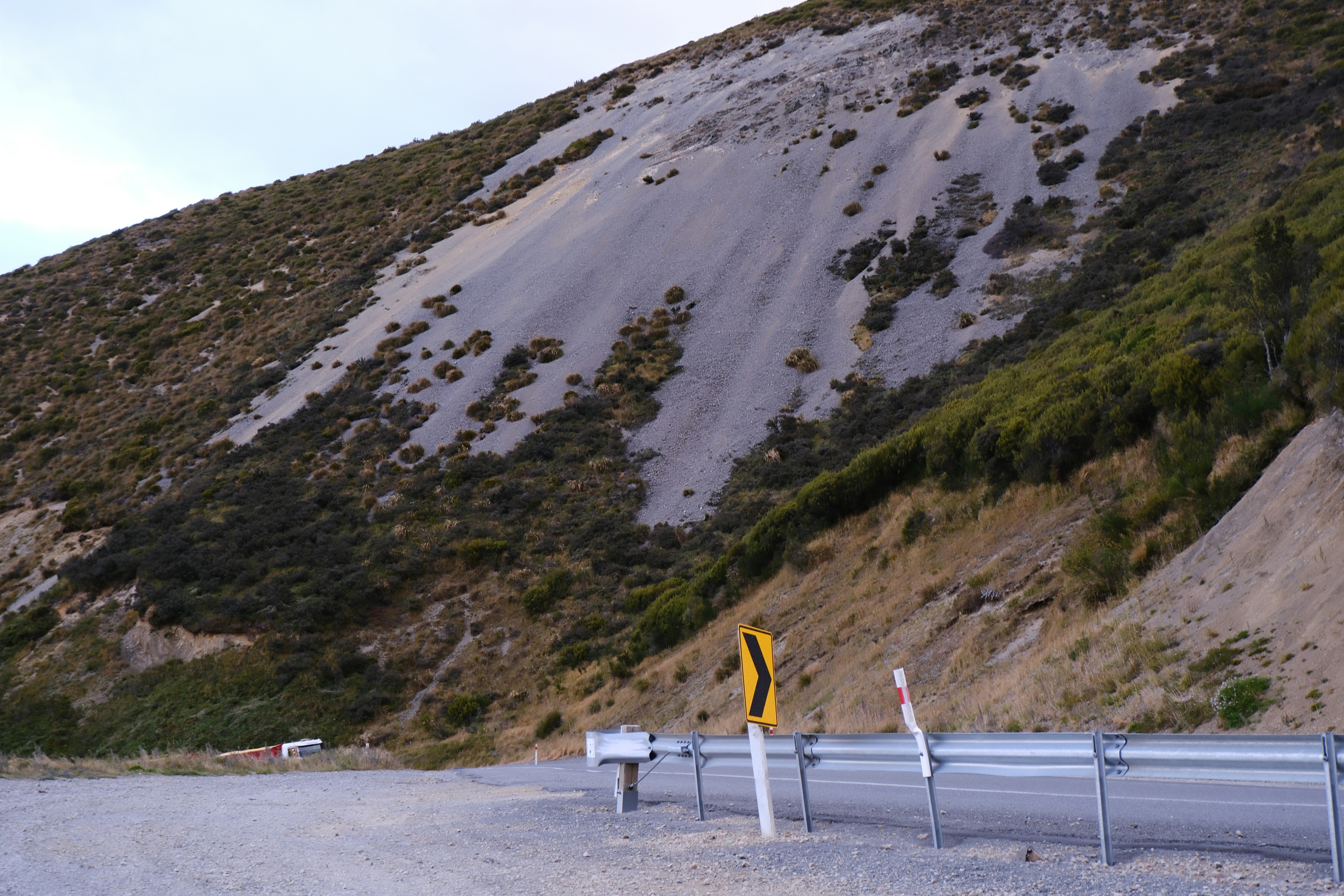 A steep, rocky hillside with sparse vegetation and a road.