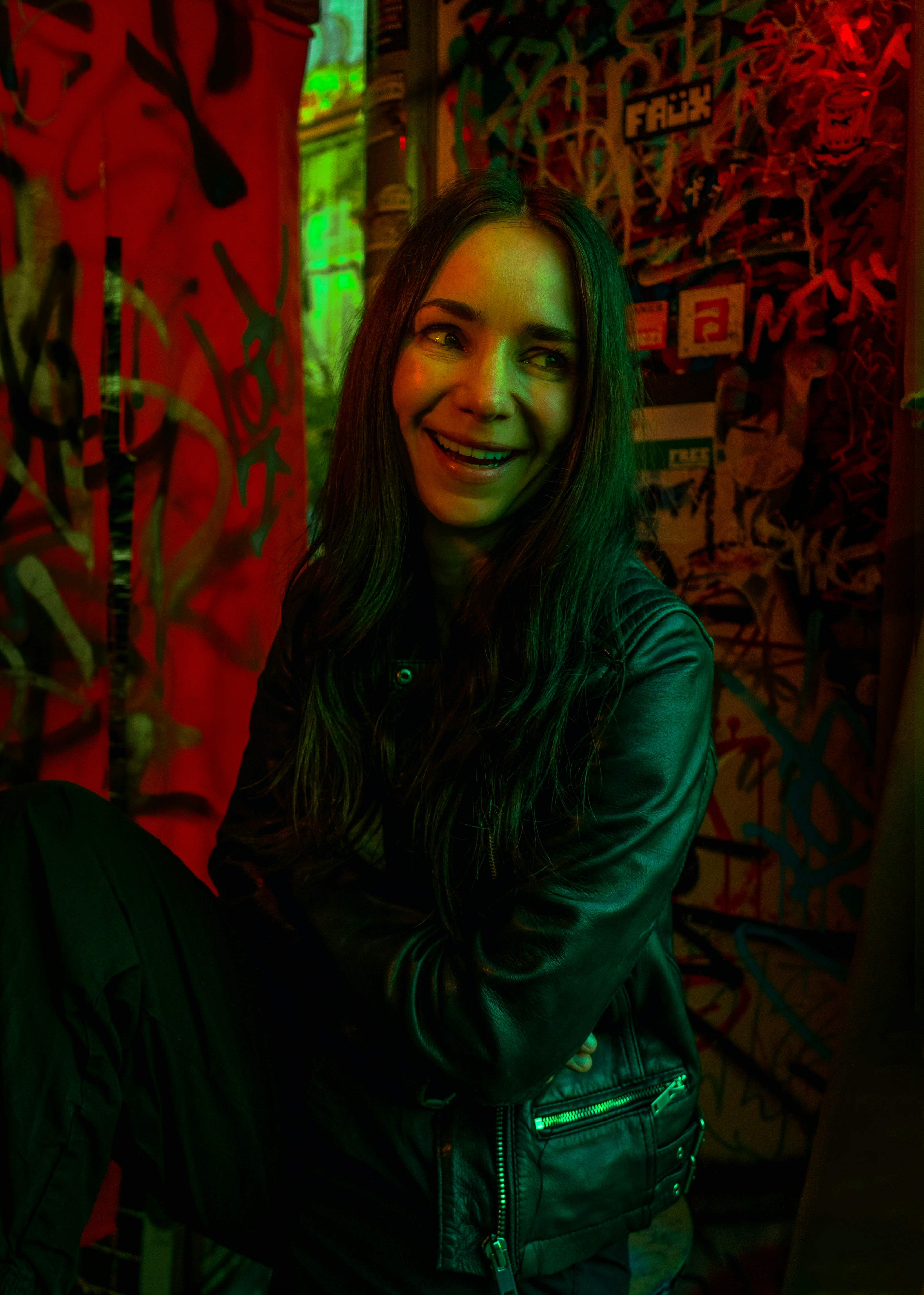 Young woman smiles in a dimly lit room with graffiti.