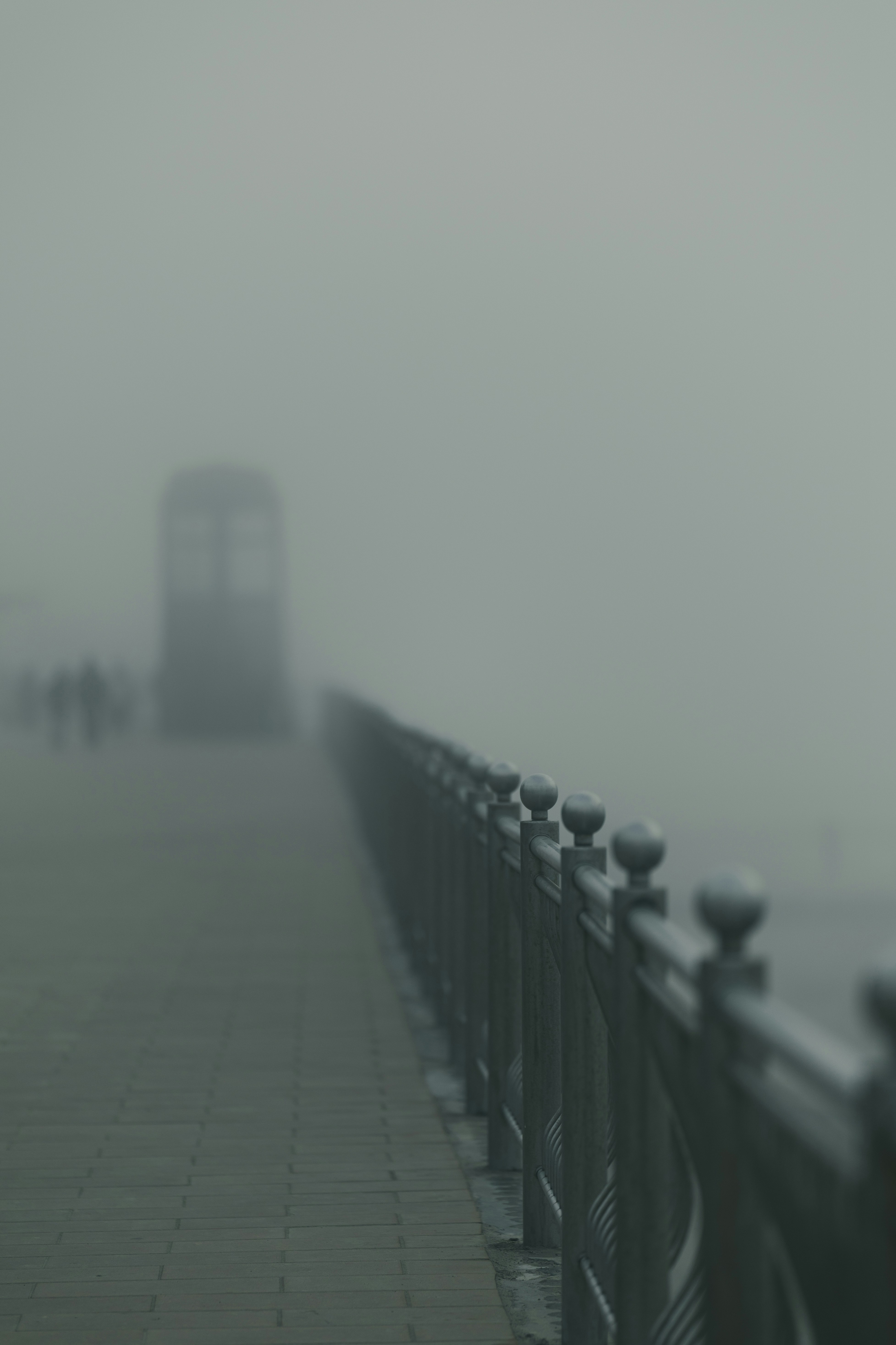 A foggy pier with a railing and distant figures.