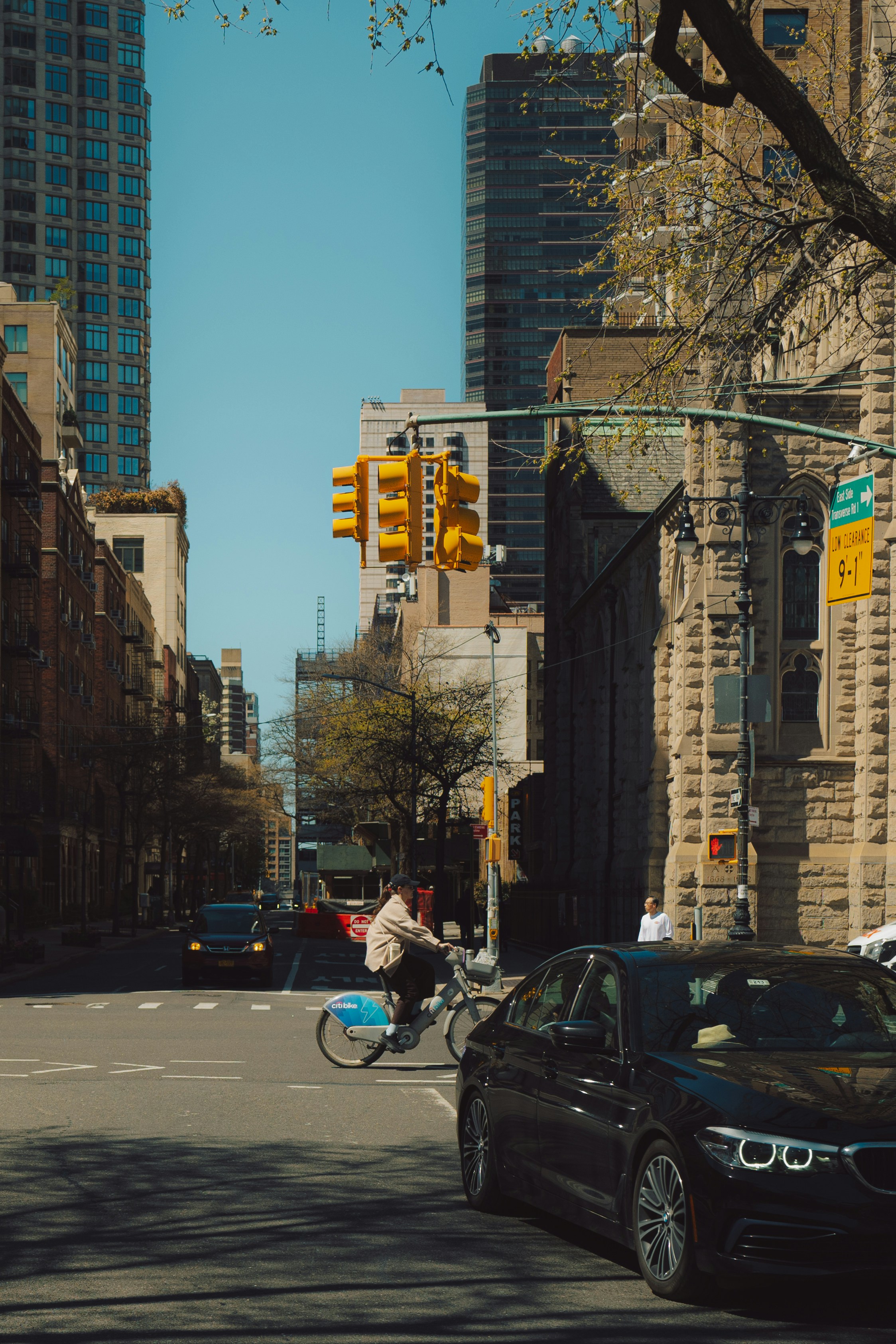 Cyclist crosses a city street with cars and buildings.