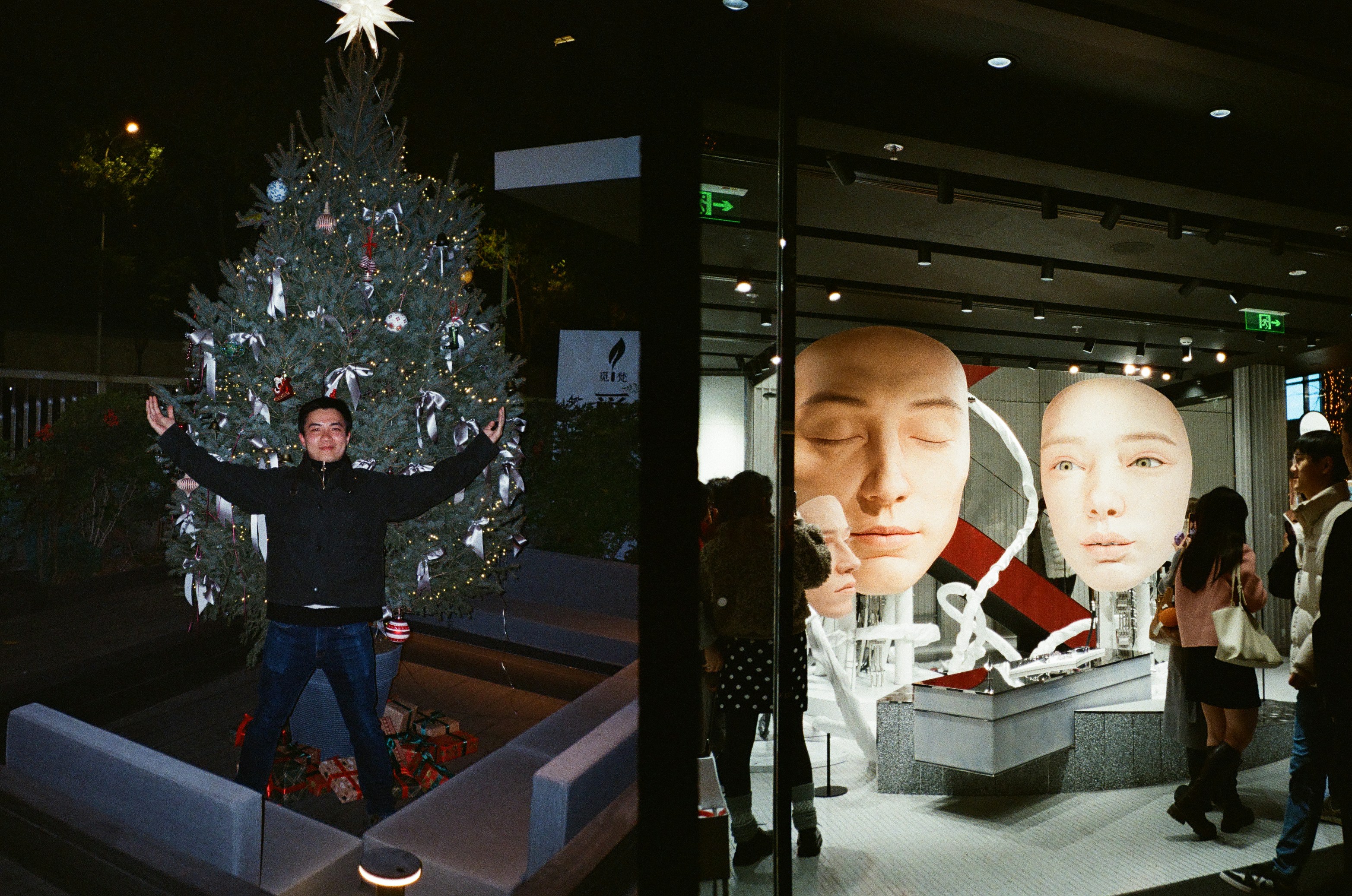 Man poses by christmas tree, people look at art display.