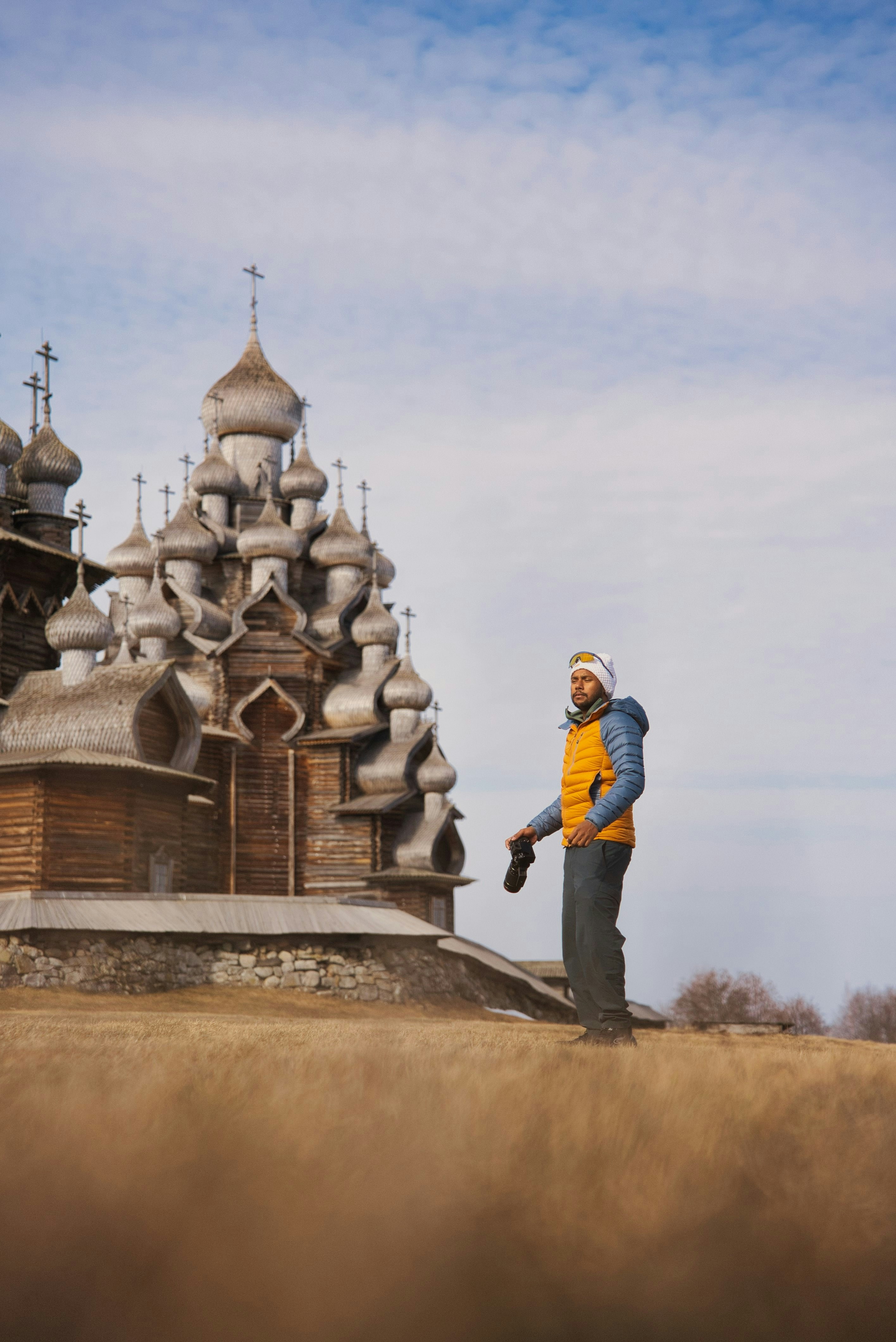 Uomo con la macchina fotografica si trova su una collina erbosa vicino a una chiesa di legno.