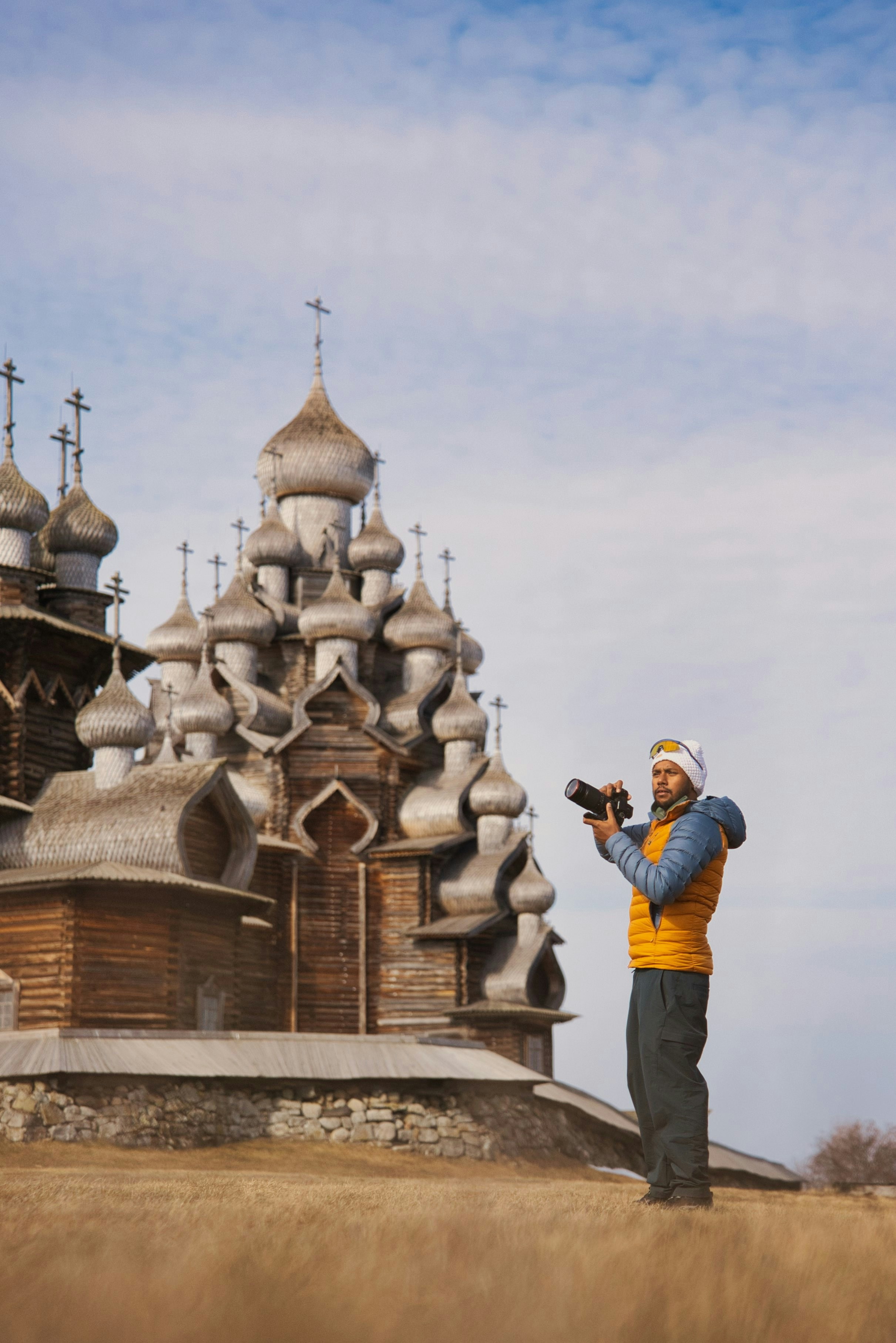 Uomo fotografa una chiesa di legno in un campo erboso