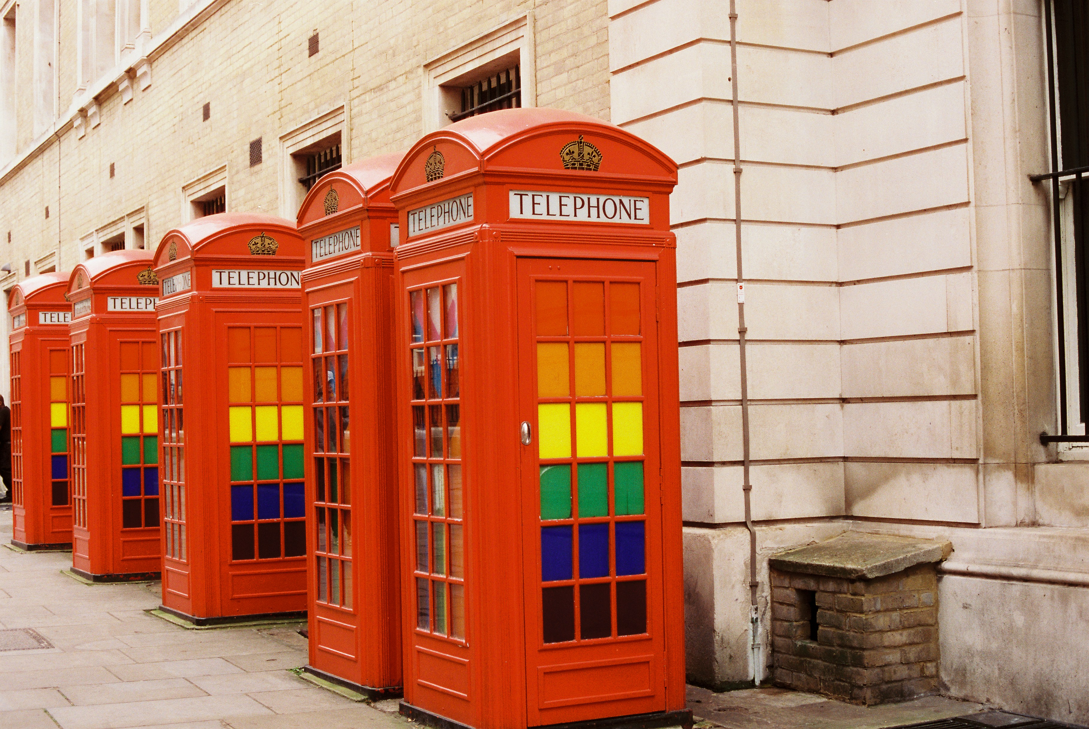 Four red telephone booths with rainbow colored windows
