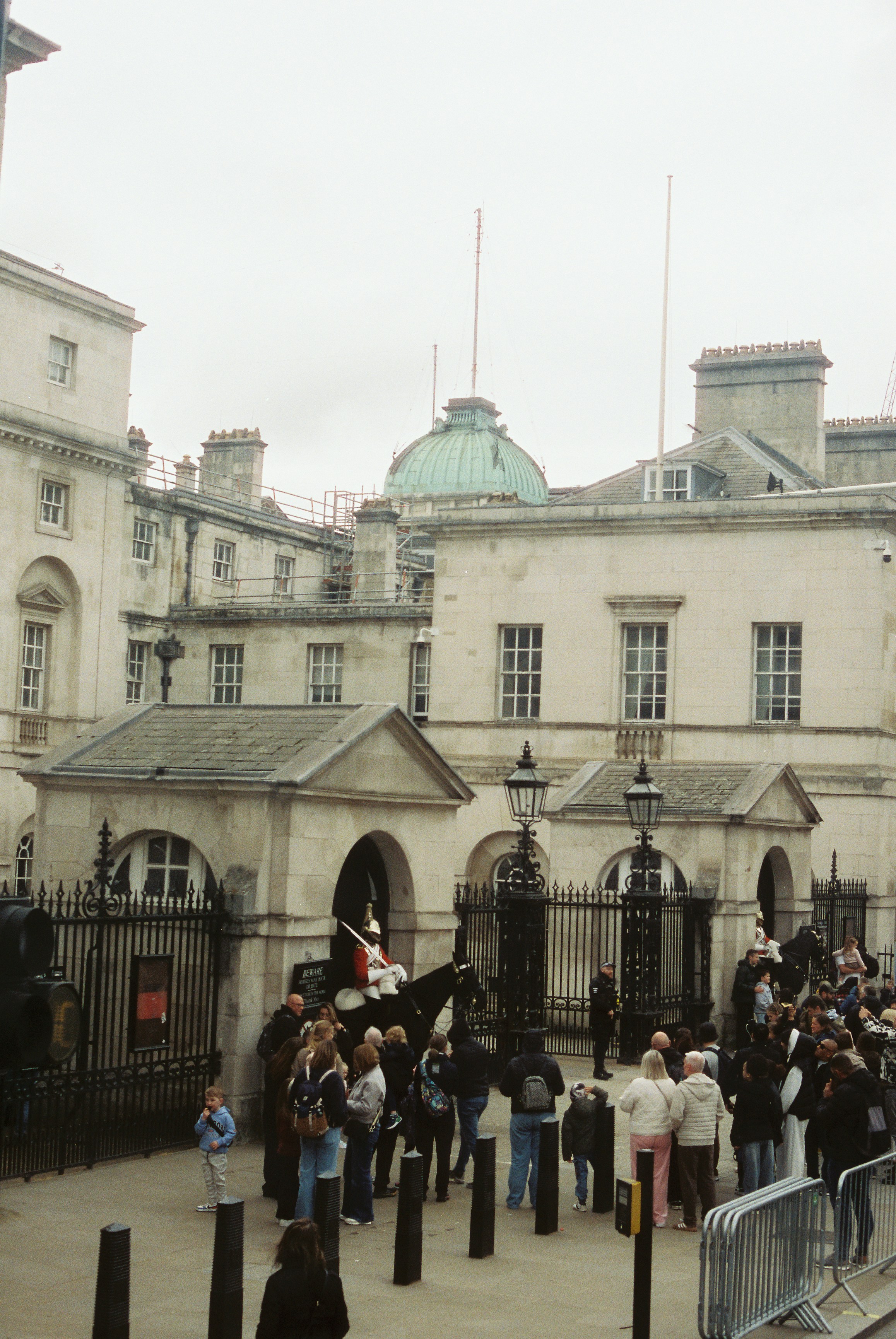 A multidão observa um guarda de cavalos na entrada de um prédio.