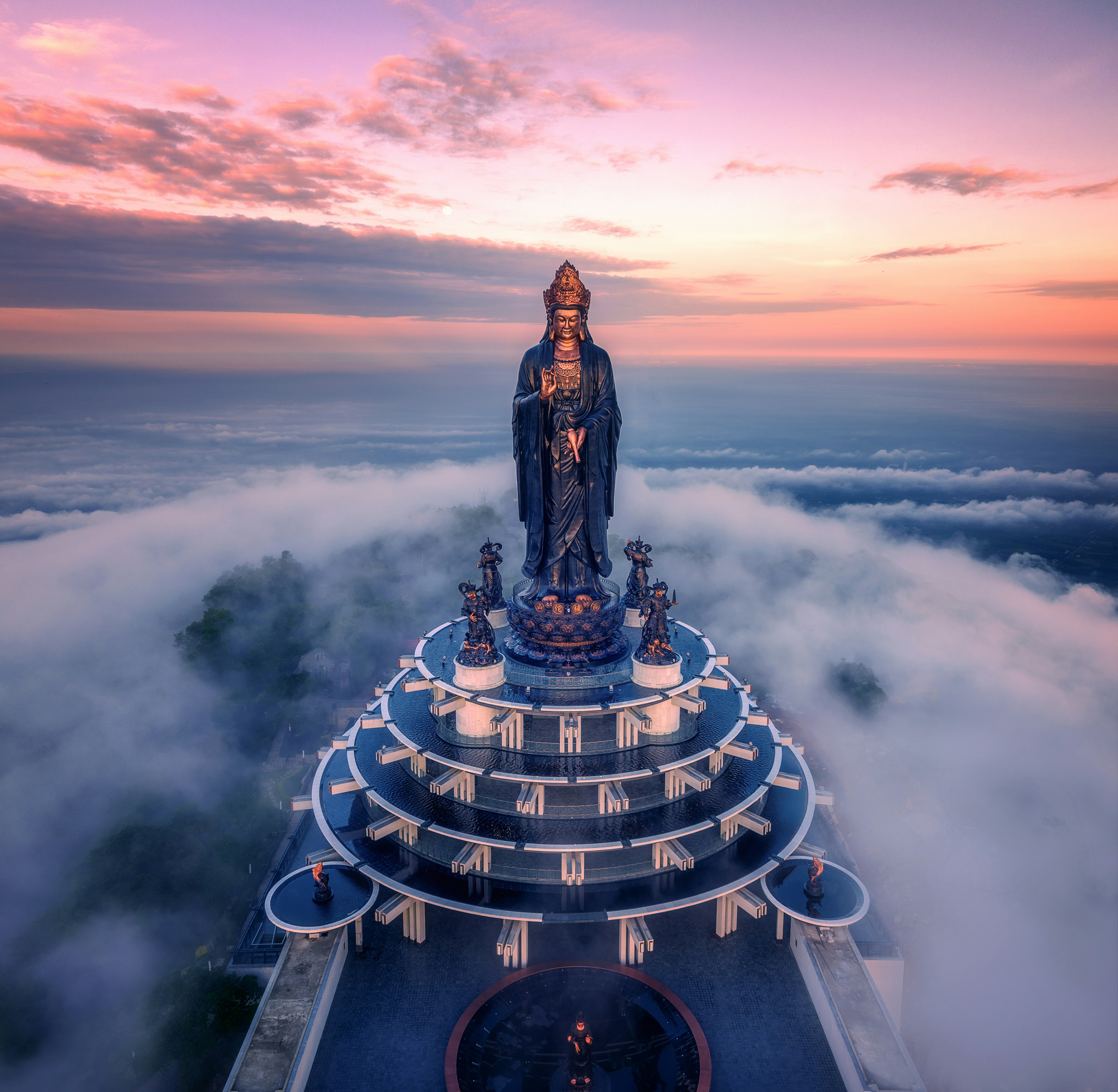 Uma majestosa estátua está no topo de uma plataforma em degraus acima das nuvens.