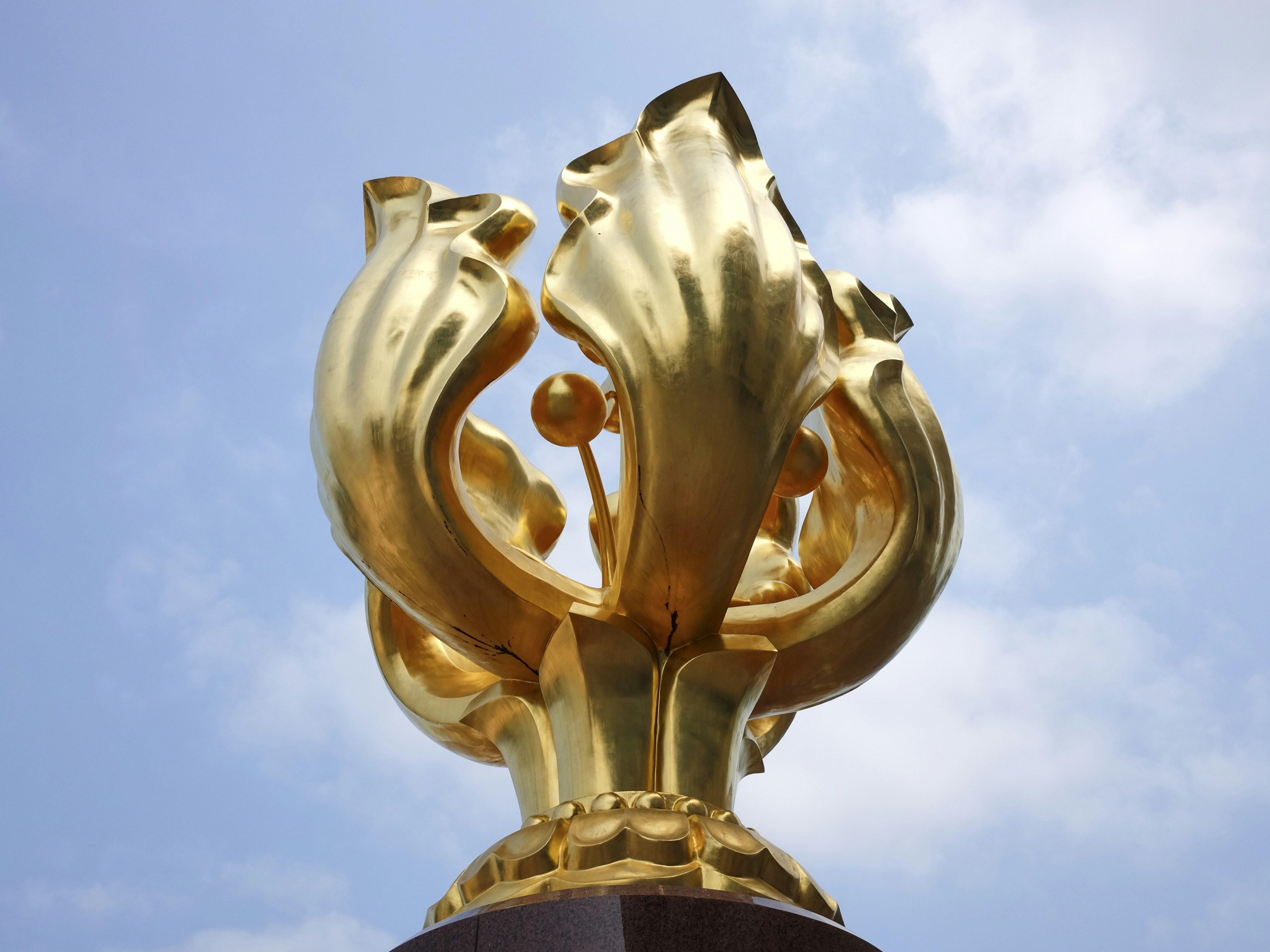 A golden abstract sculpture against a blue sky