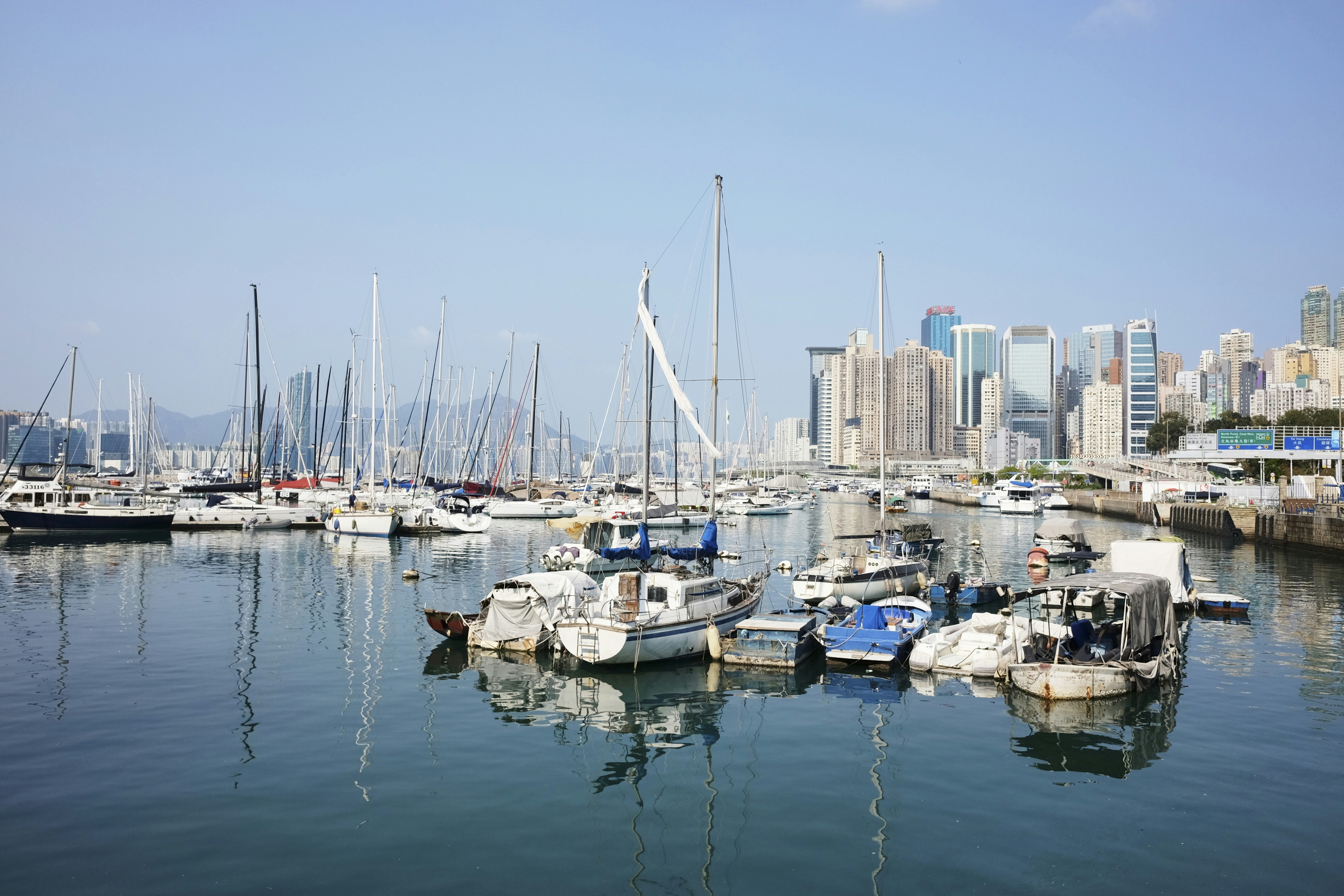 Sailboats and yachts docked in a harbor with city skyline.