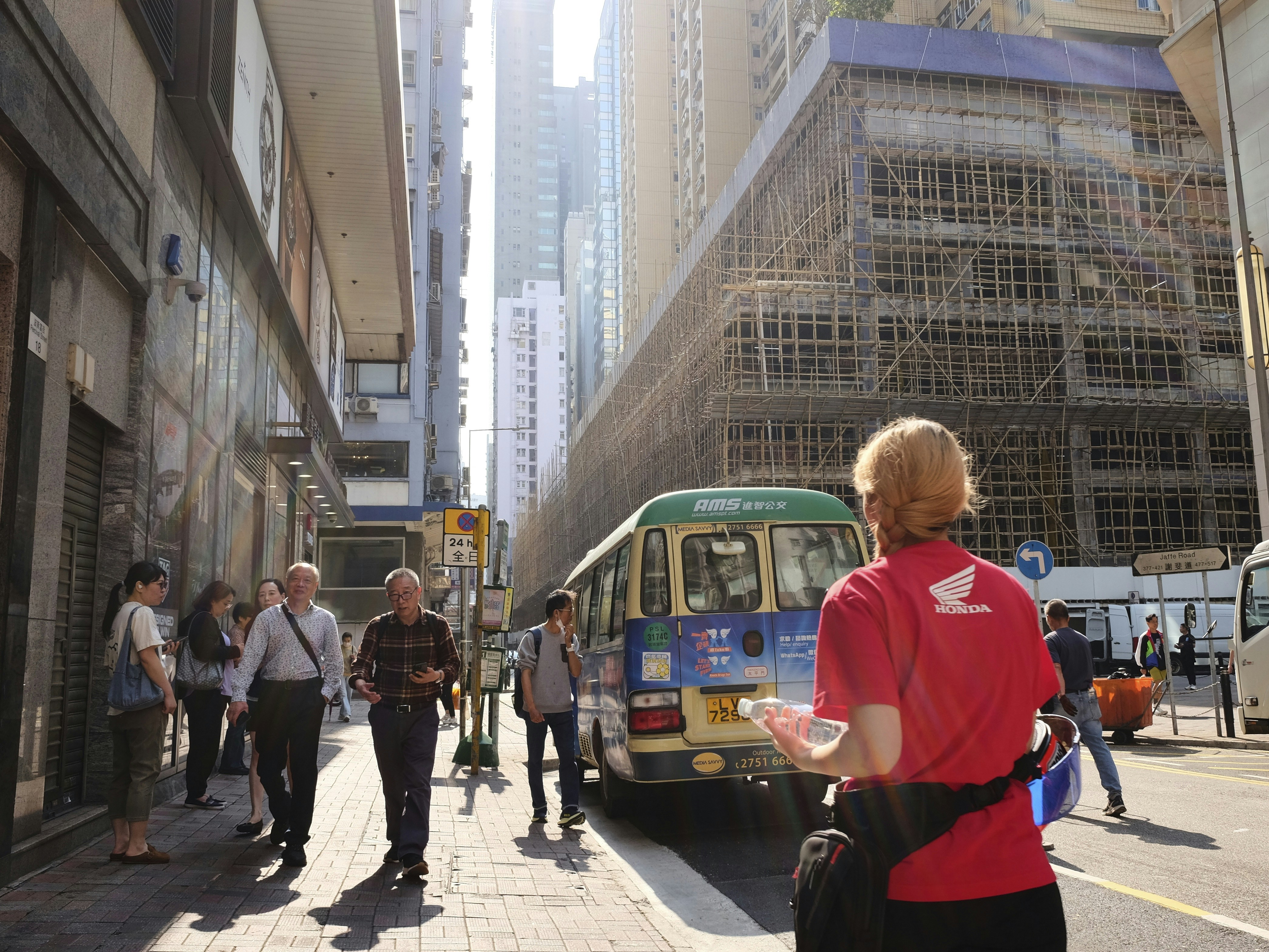 Tourists follow guide down sunny city street with bus.