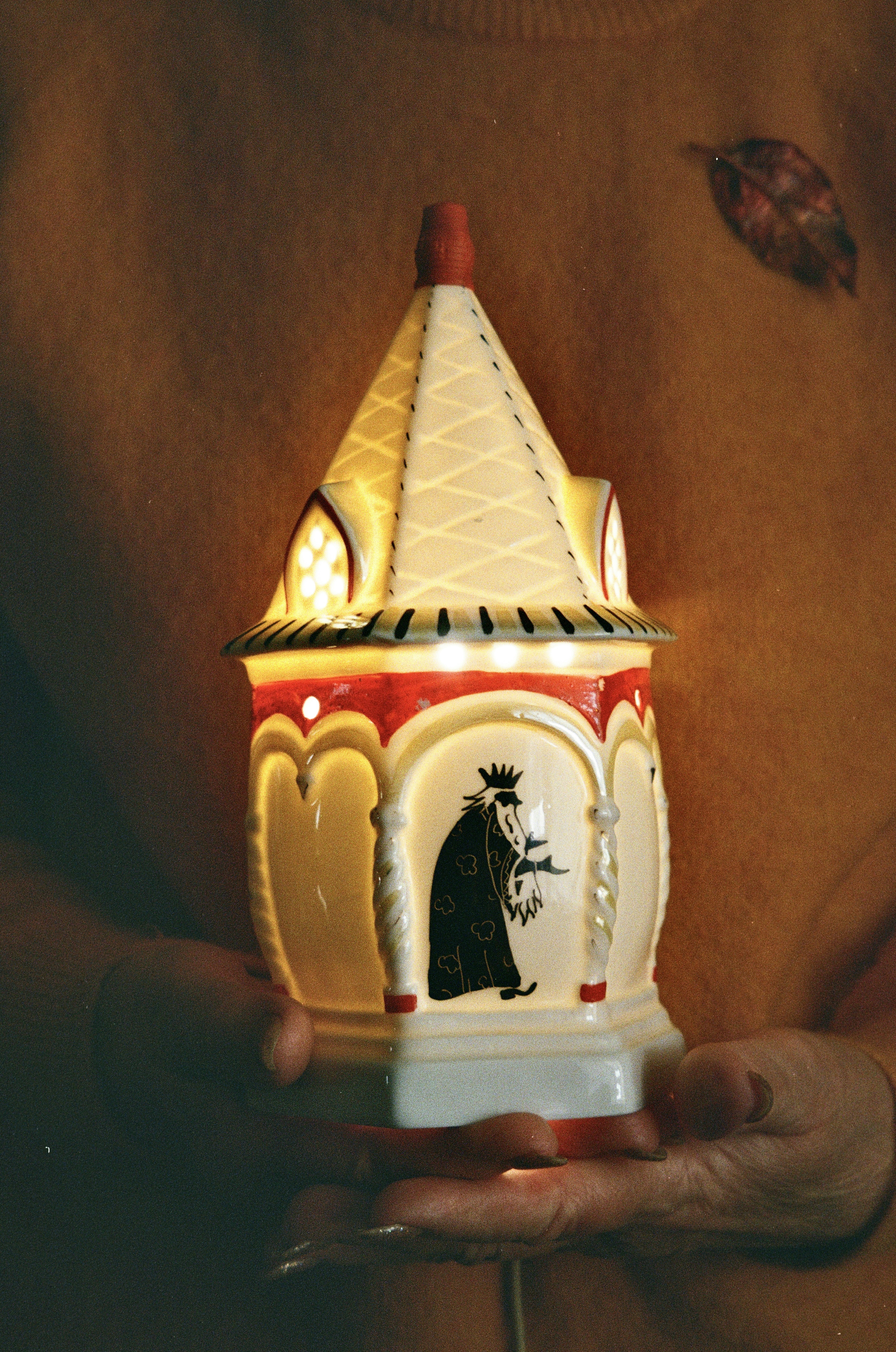 Person holding a decorative illuminated building with a king's figure