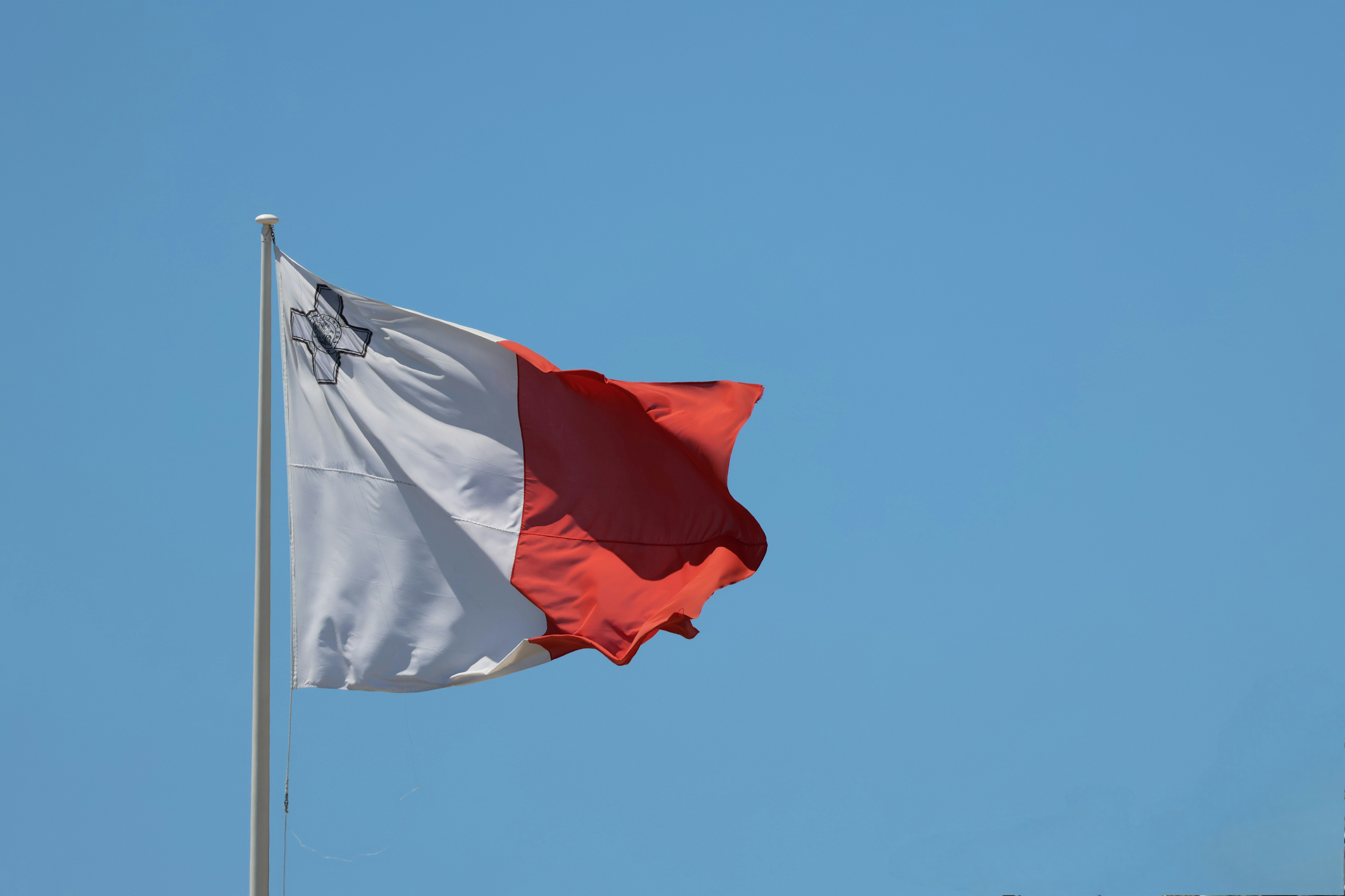 Le drapeau de Malte flotte contre un ciel bleu clair.