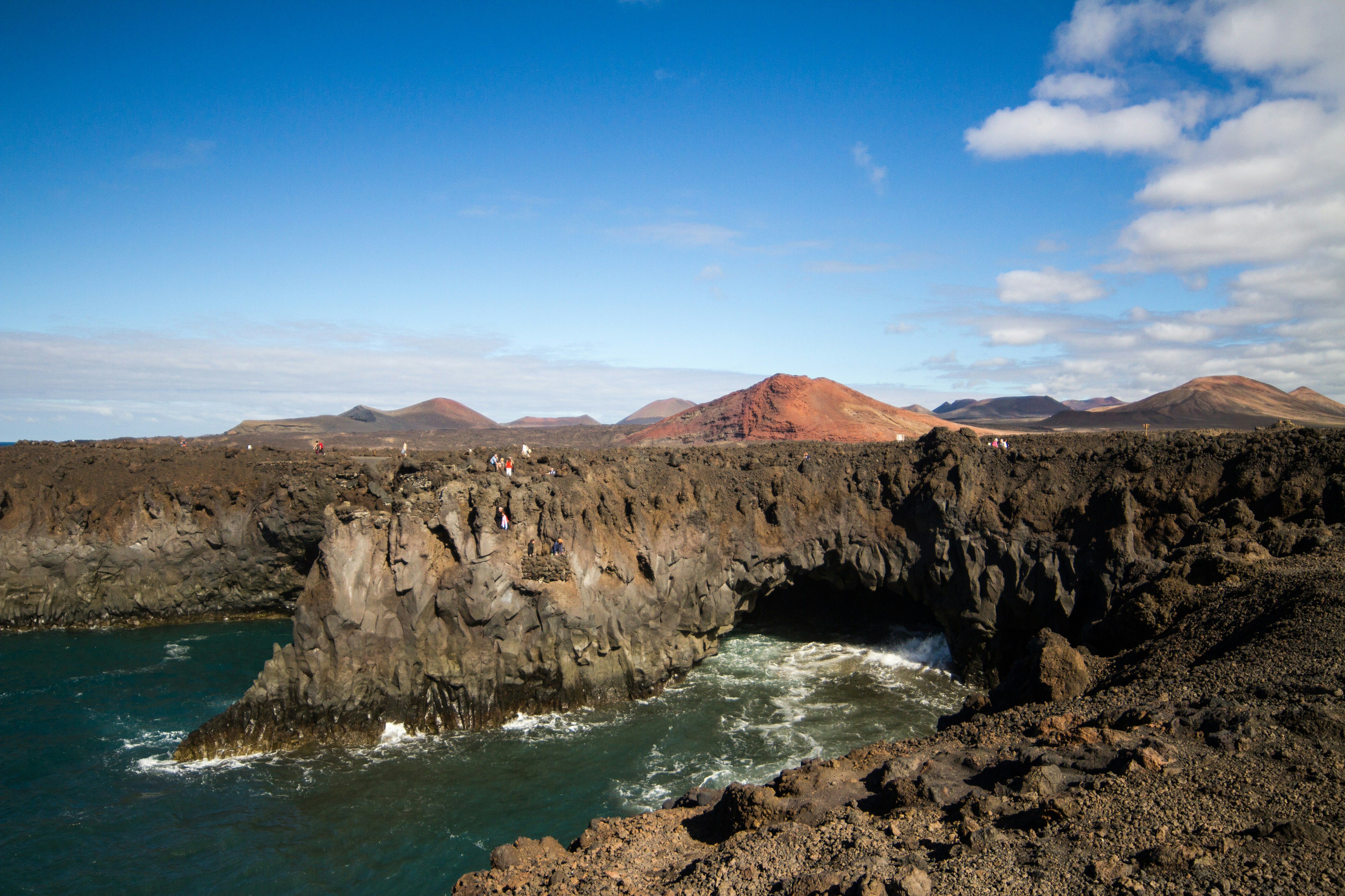 Rocky coastline with a sea arch and distant mountains.