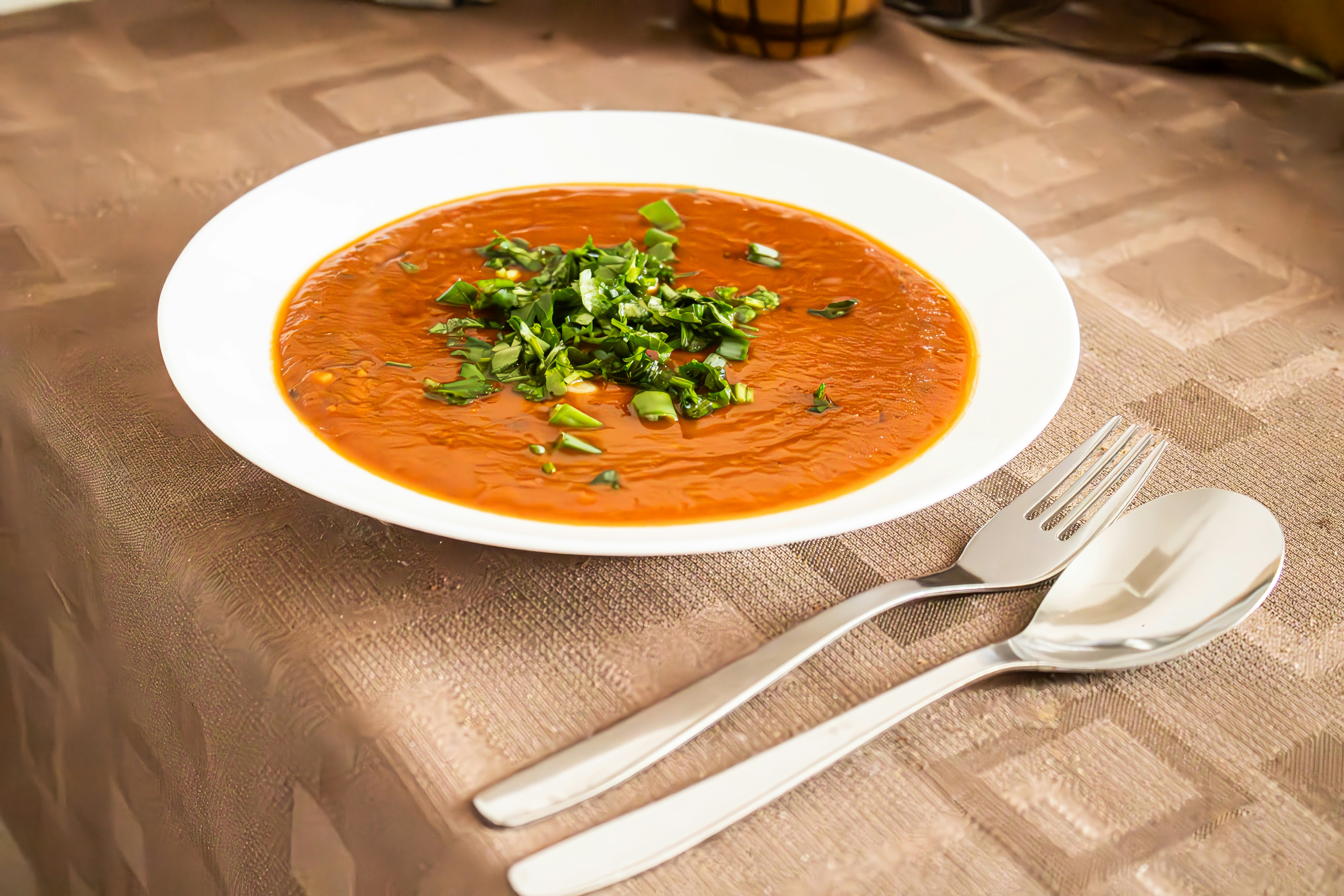新鮮なハーブとカトラリーを添えたトマトスープのボウル