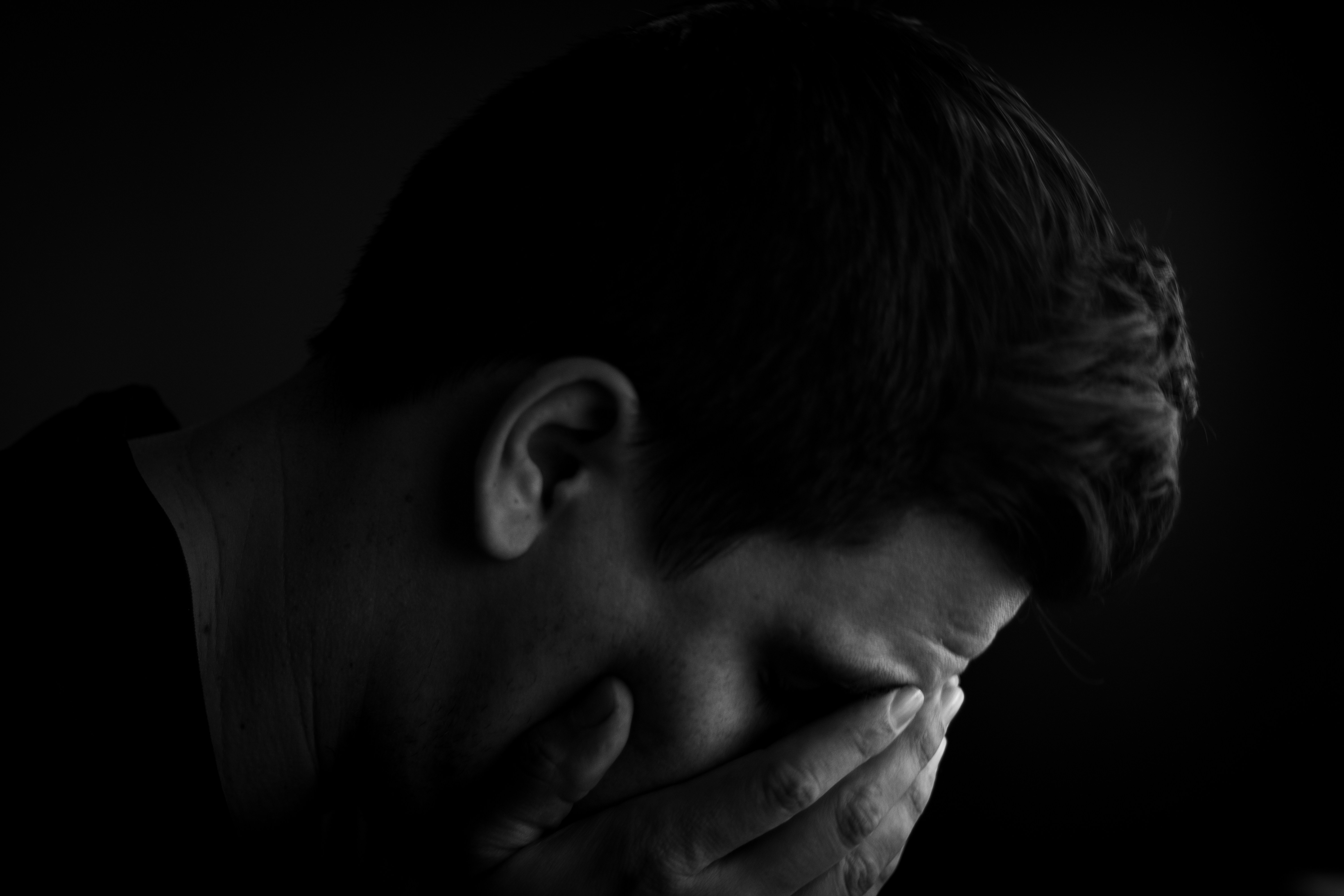 Hombre con la cabeza entre las manos en la oscuridad