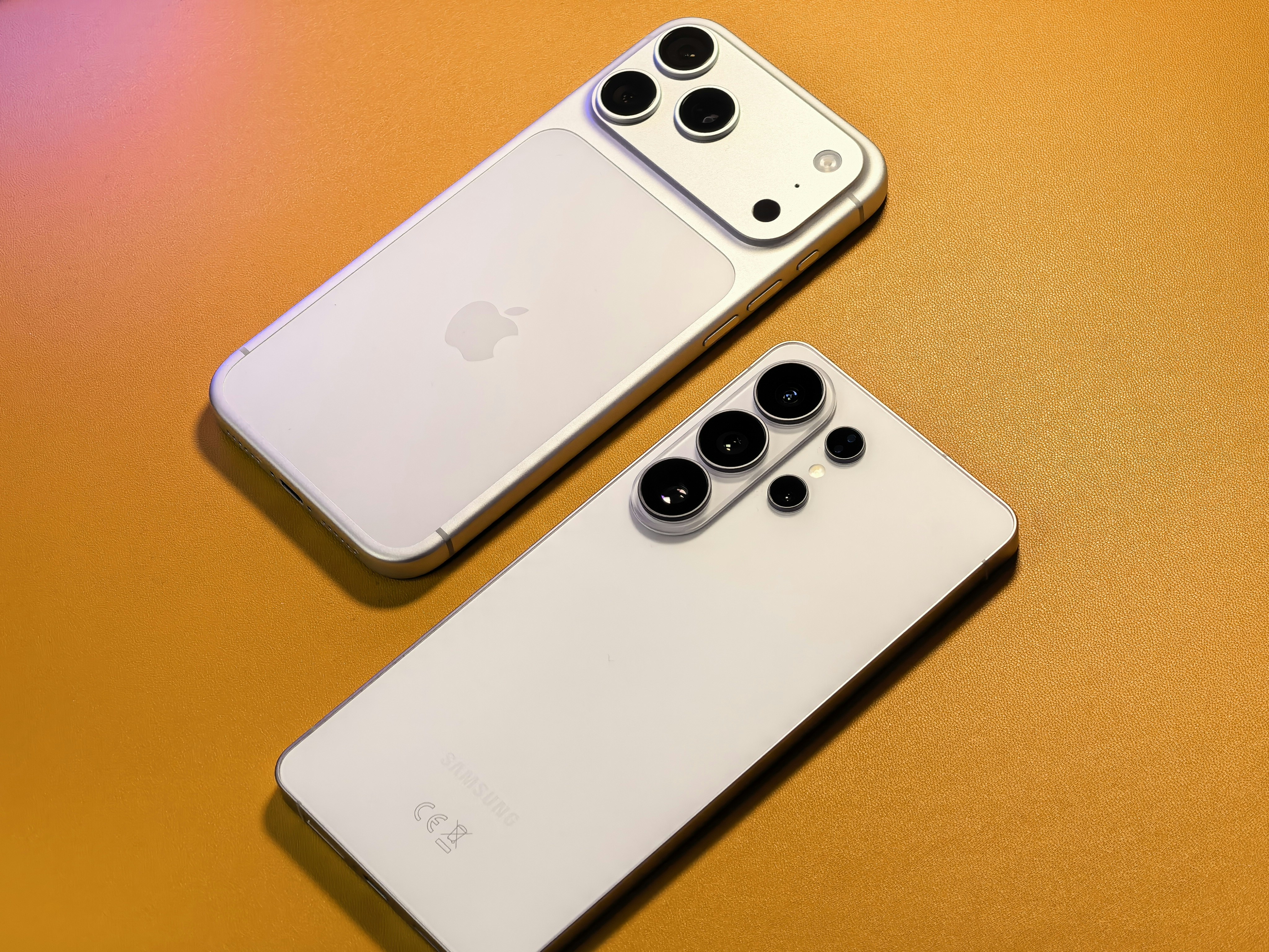 Two smartphones with multiple cameras arranged on orange surface