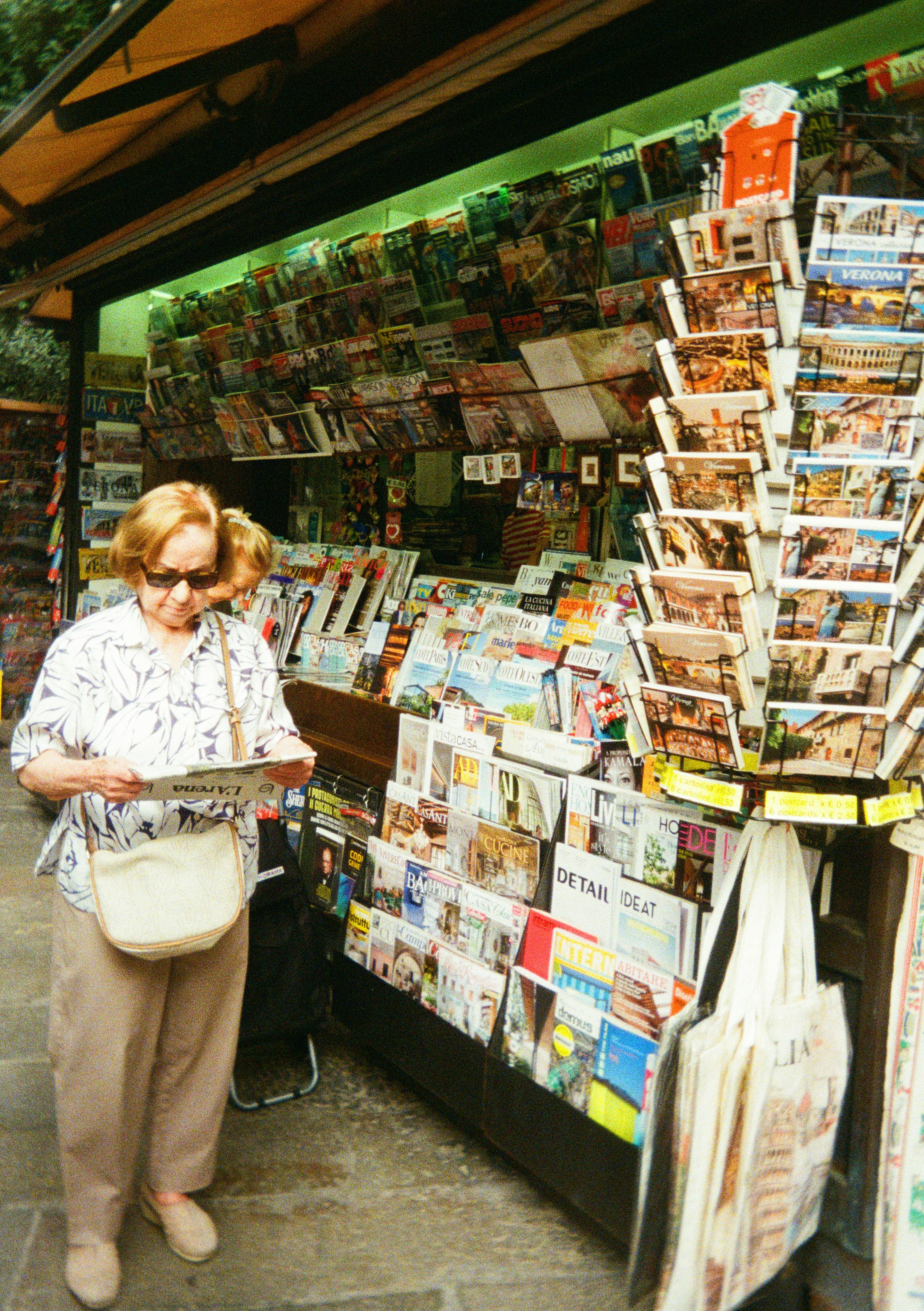 Donna anziana che sfoglia riviste in un'edicola.