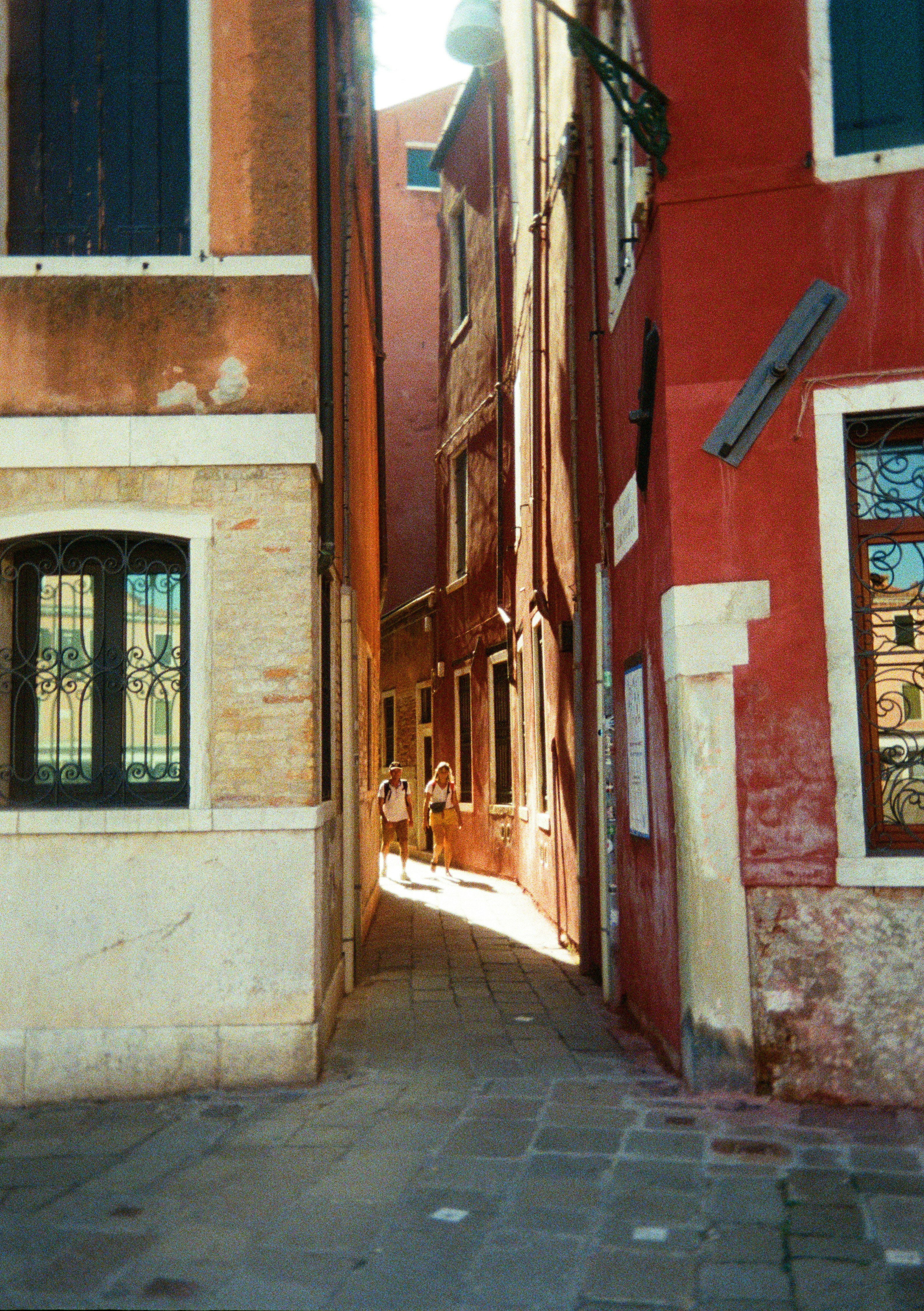 Due persone camminano lungo un stretto vicolo veneziano.
