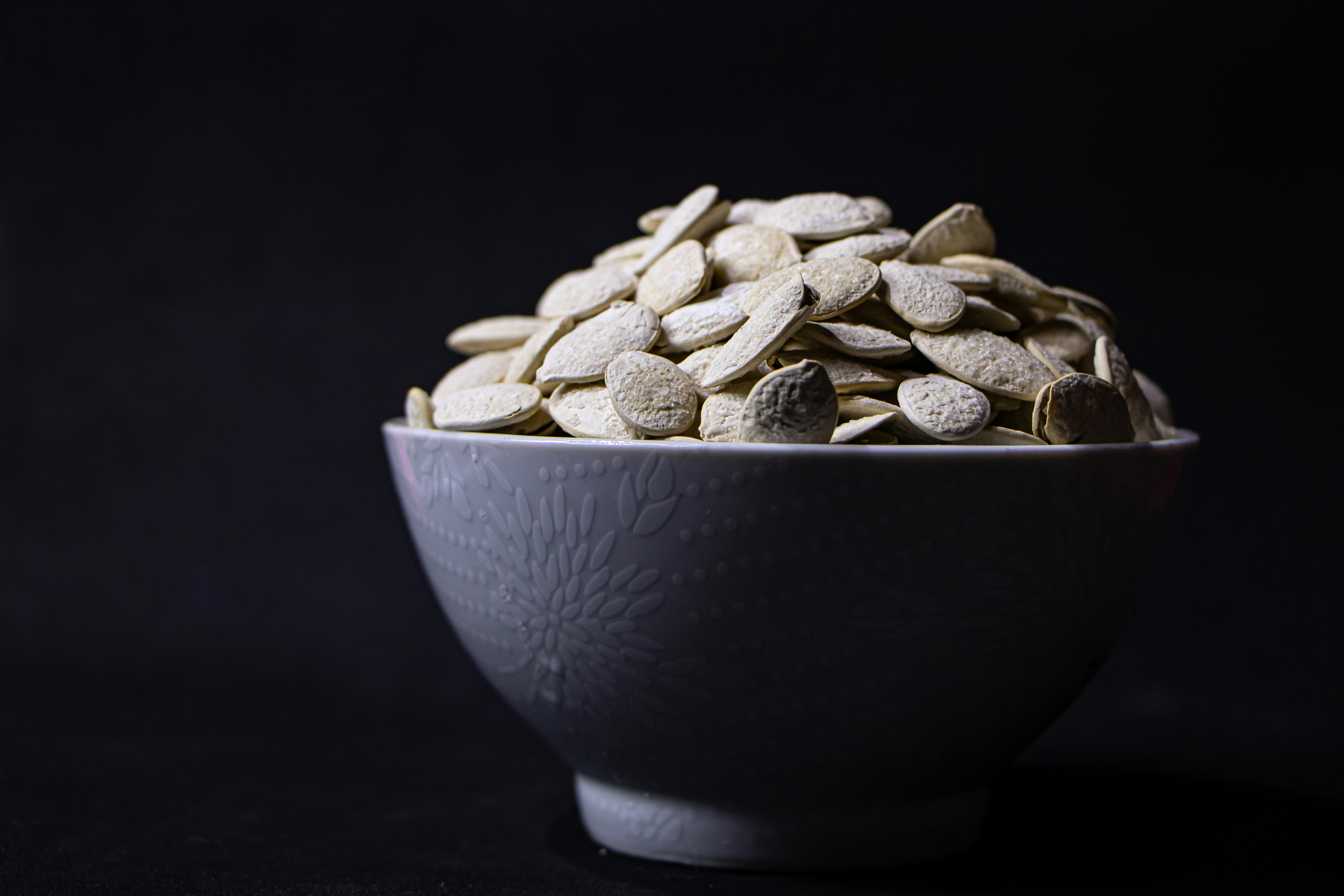 A bowl filled with pumpkin seeds on a dark background