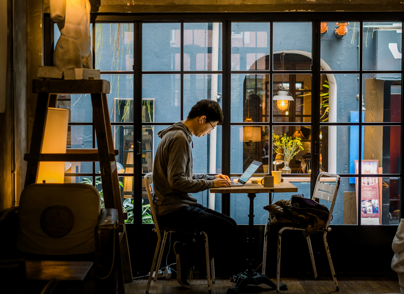 Traveller working on a laptop at a café table by a large window in warm evening light