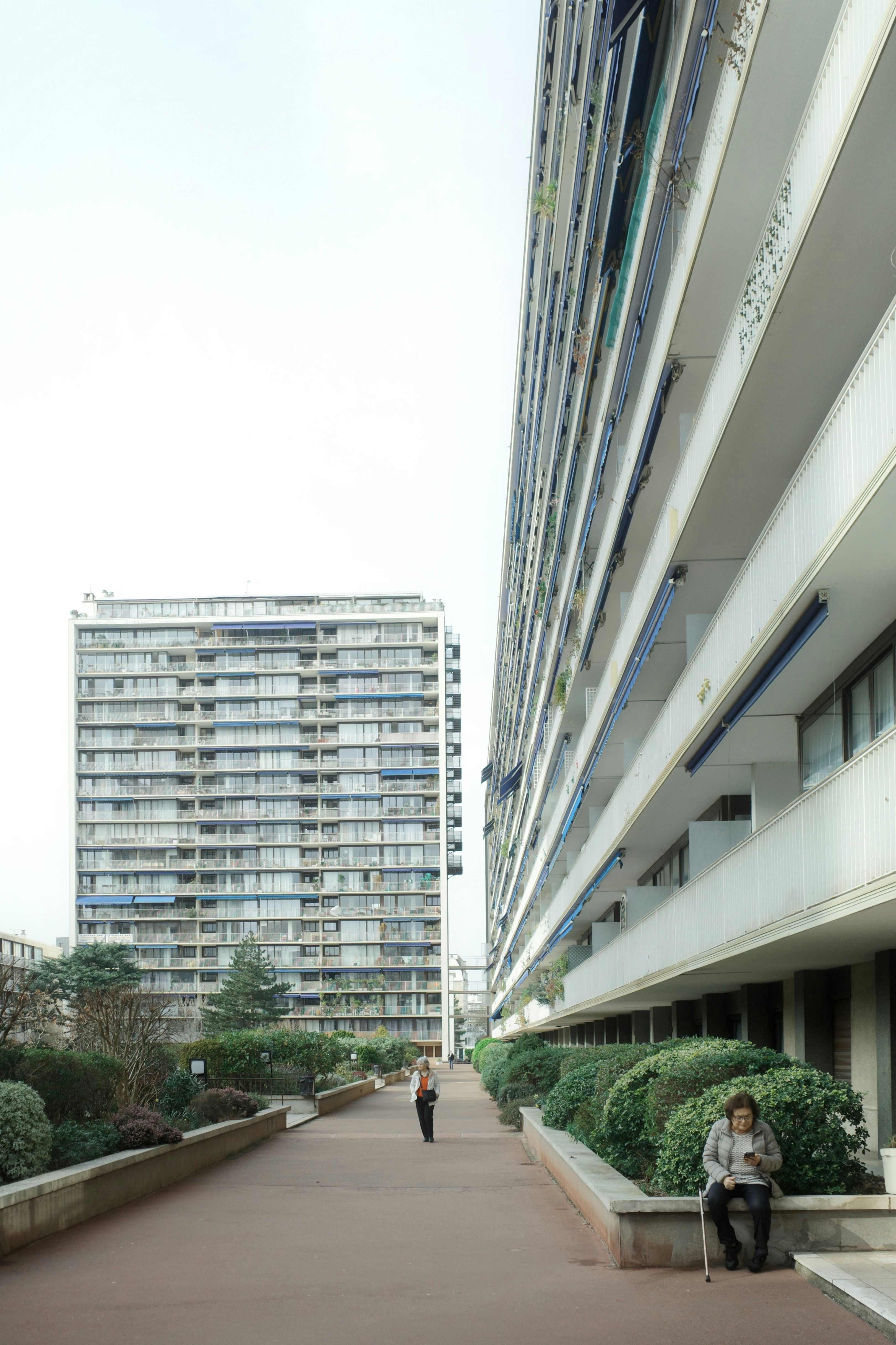 Two people walk on a path between apartment buildings.